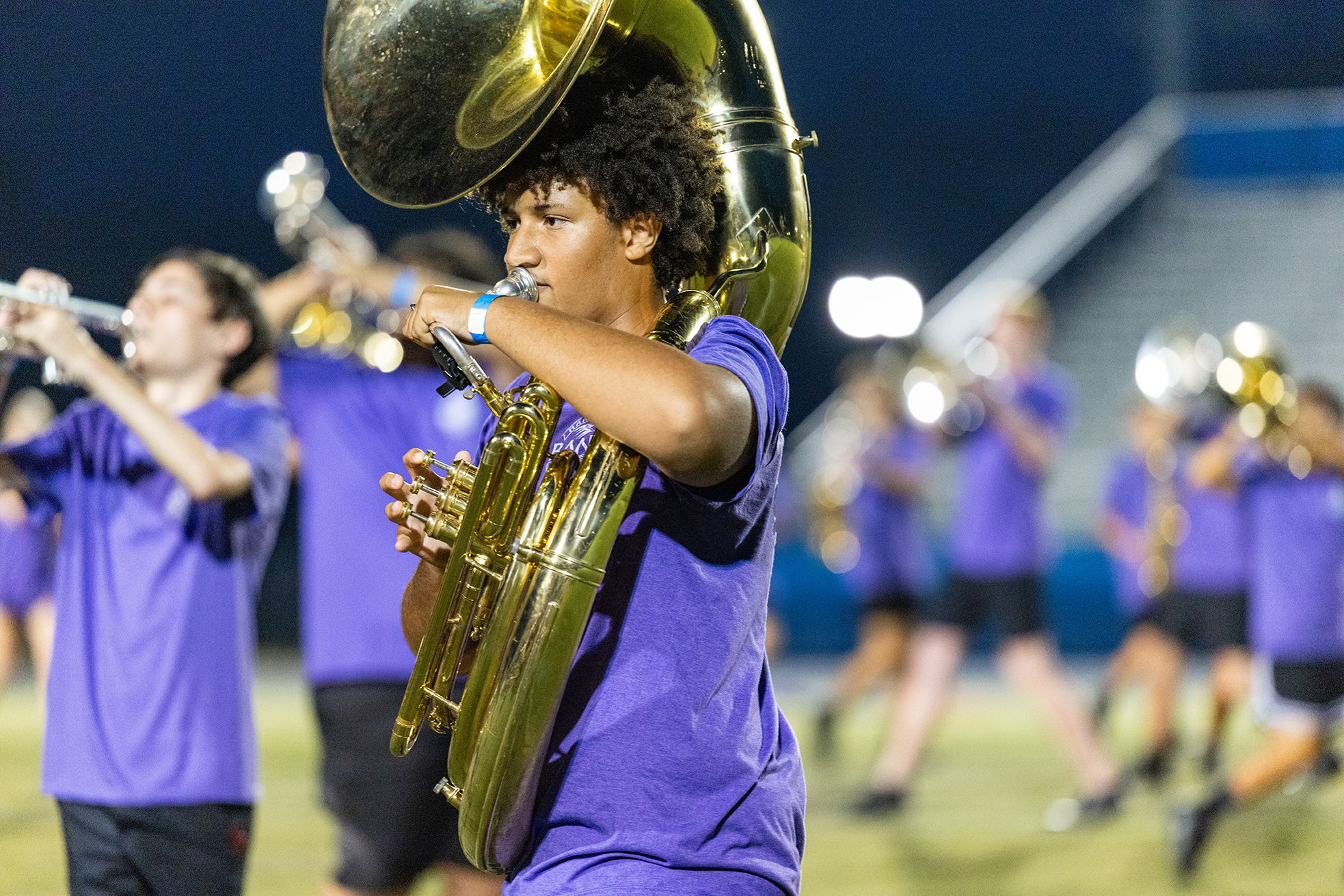 A young person plays the tuba in a school marching band during an evening performance.