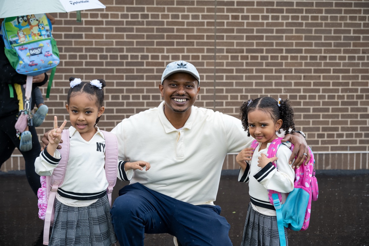 Father poses with twin daughters in the rain outside of Hoover Elementary