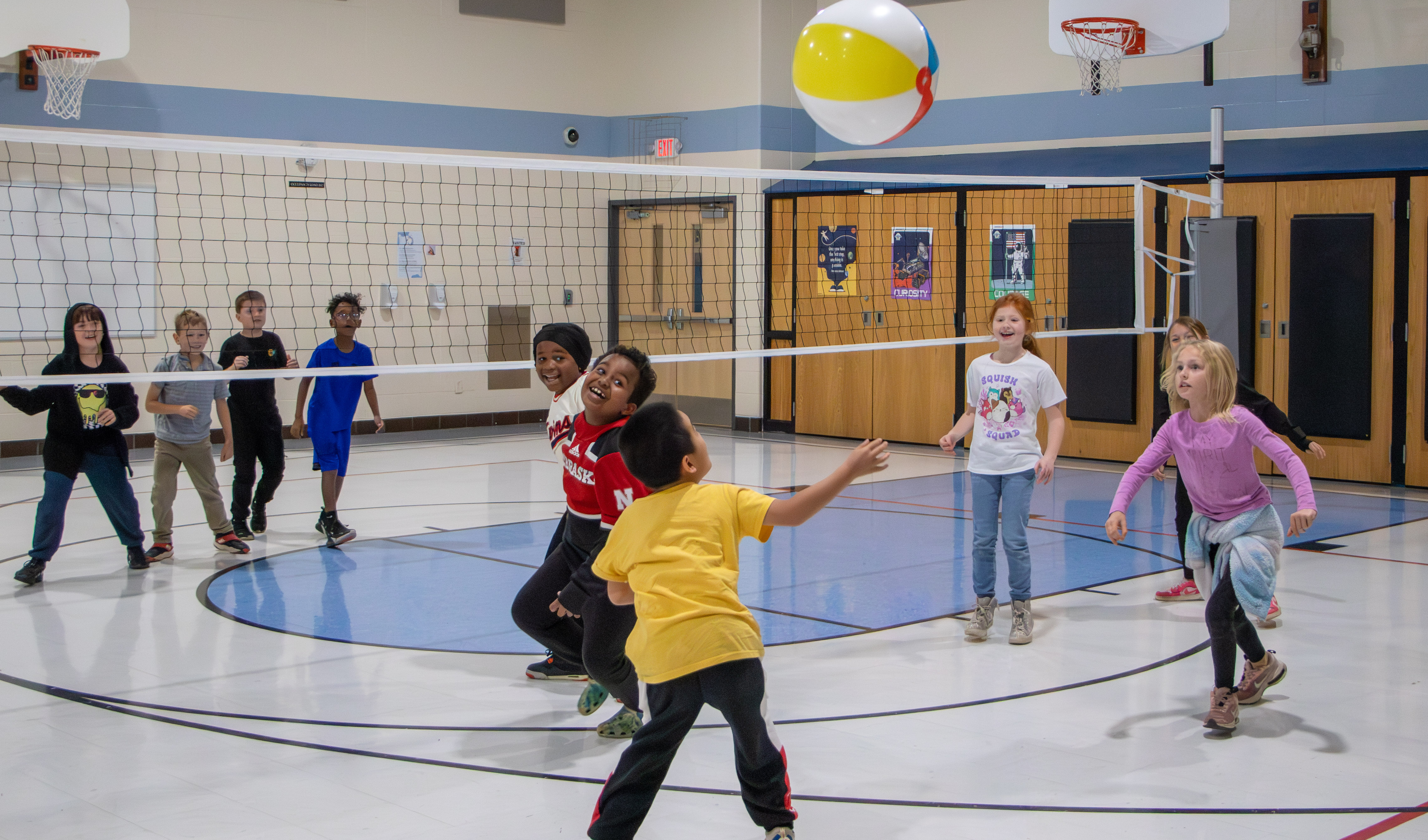 Elementary kids play volleyball with a beachball in the gym.