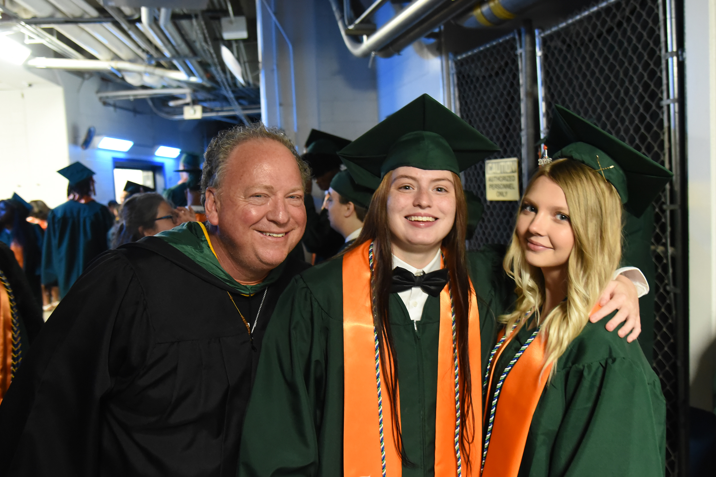A man in a black gown poses with two women in green gowns and hats. They all smile.