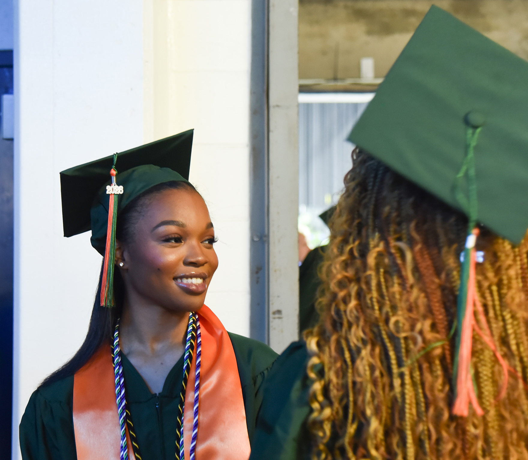 Two women in green caps, smiling, one with long curly hair and the other with a sash.
