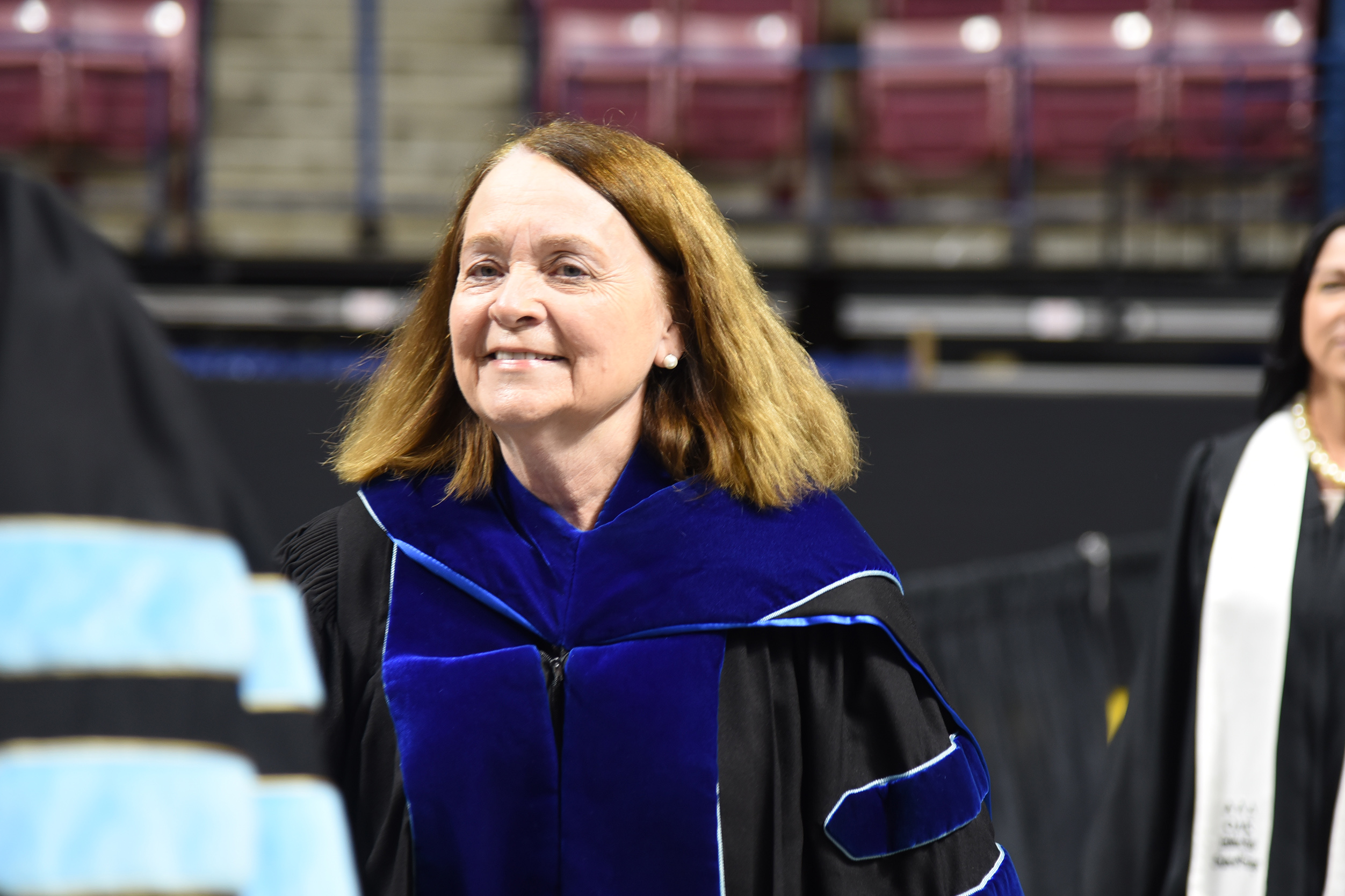 A woman with blonde hair and a smile stands in a blue and black gown at an event.