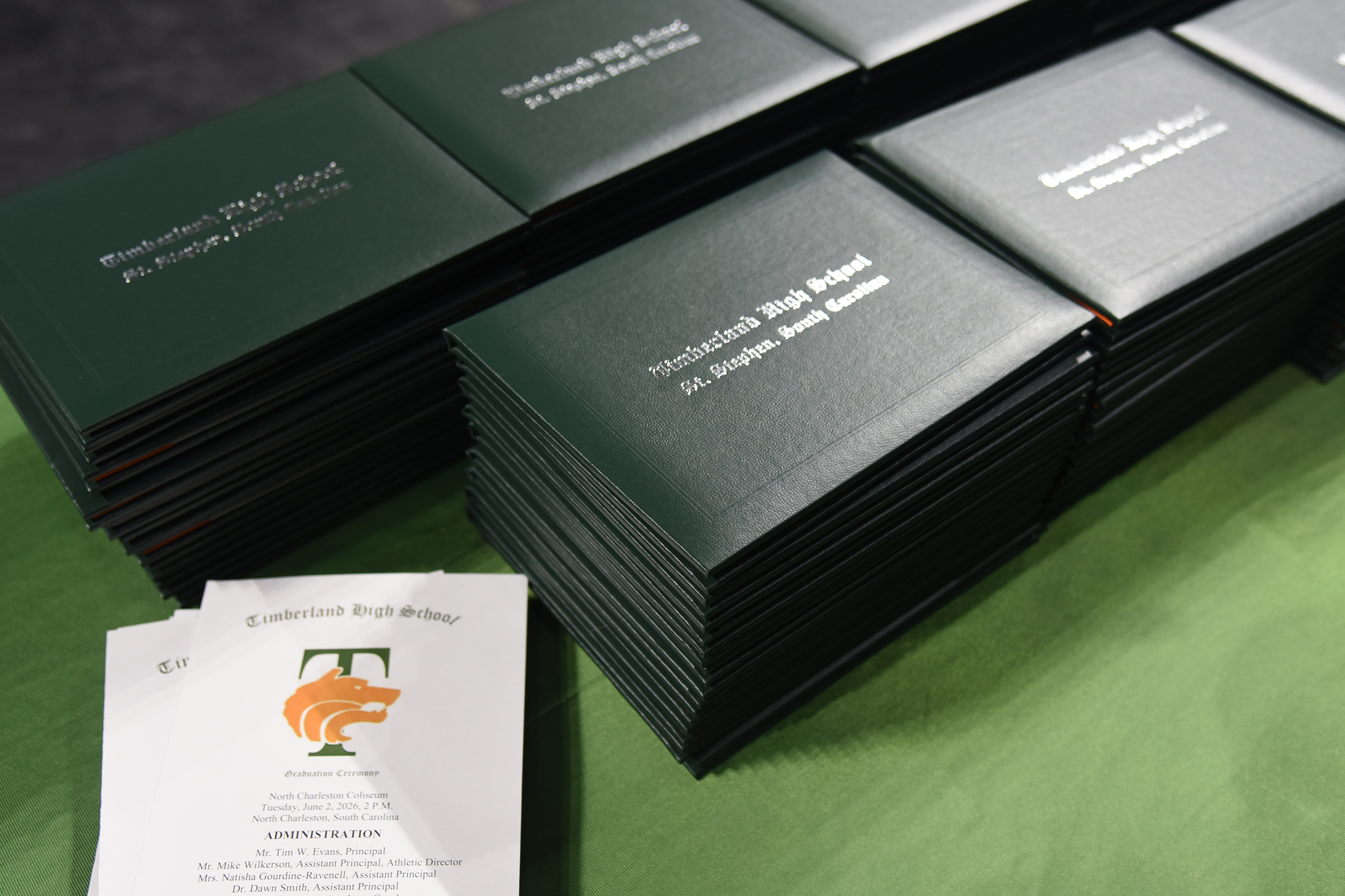 A pile of black folders, each with white text, is on a green table. A single white folder is placed to the left.