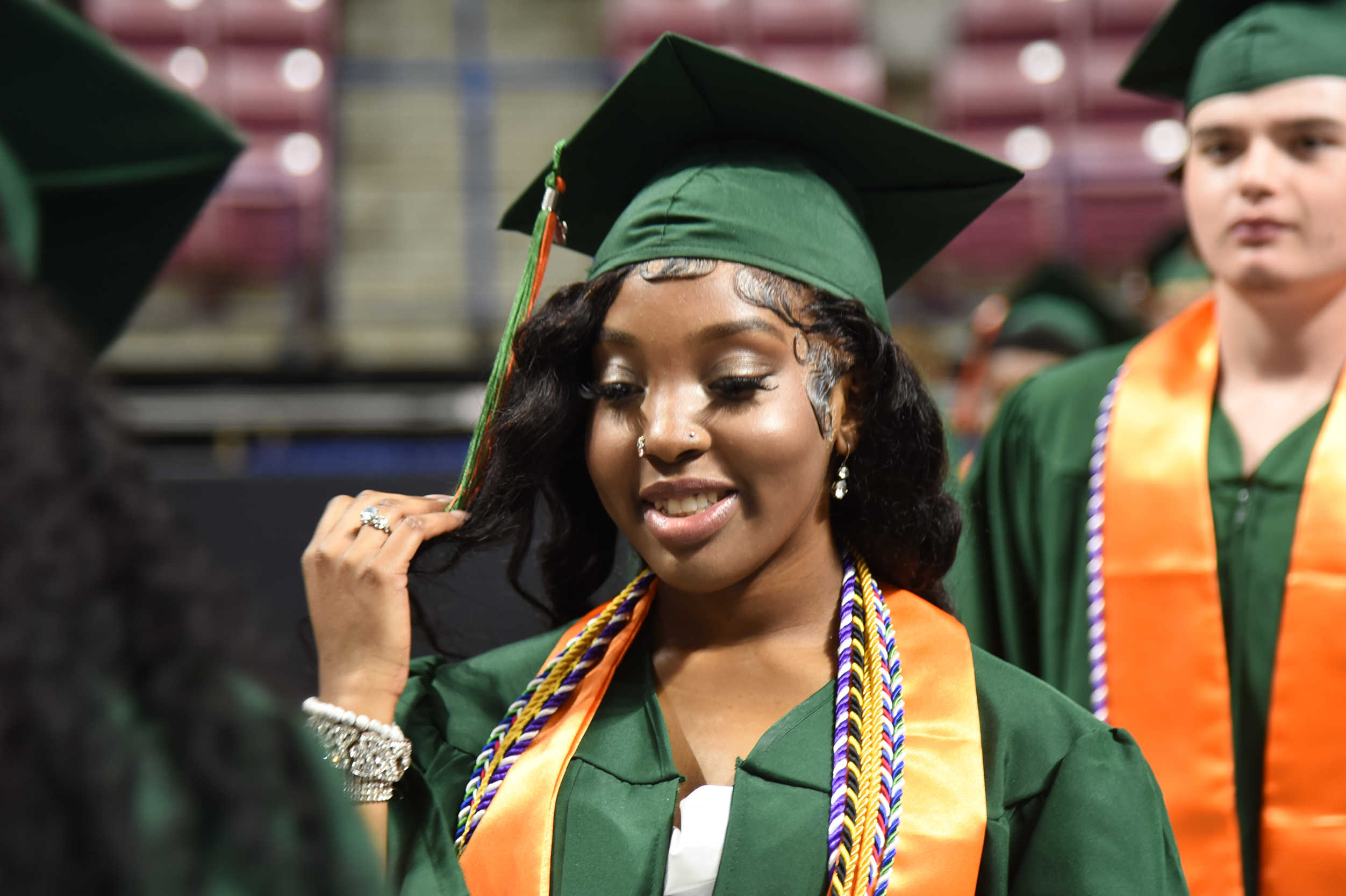 A woman with a green cap and gown smiles at a graduation ceremony.