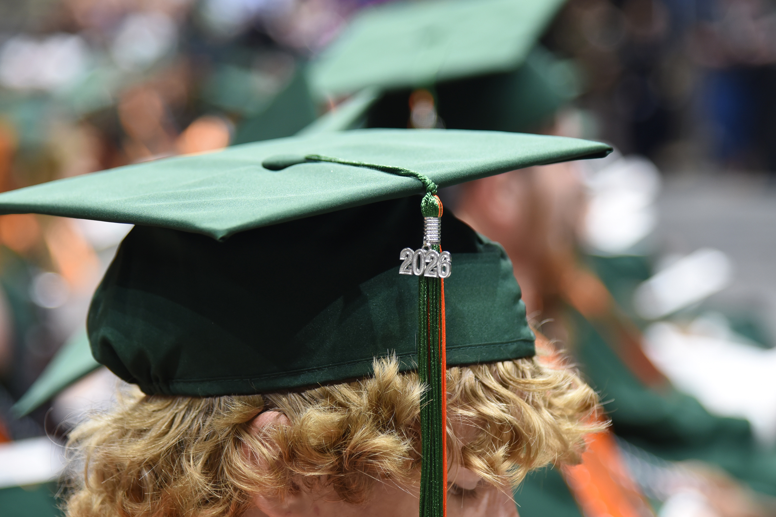 A person with light hair wears a green graduation cap, with the tassel hanging down the back.