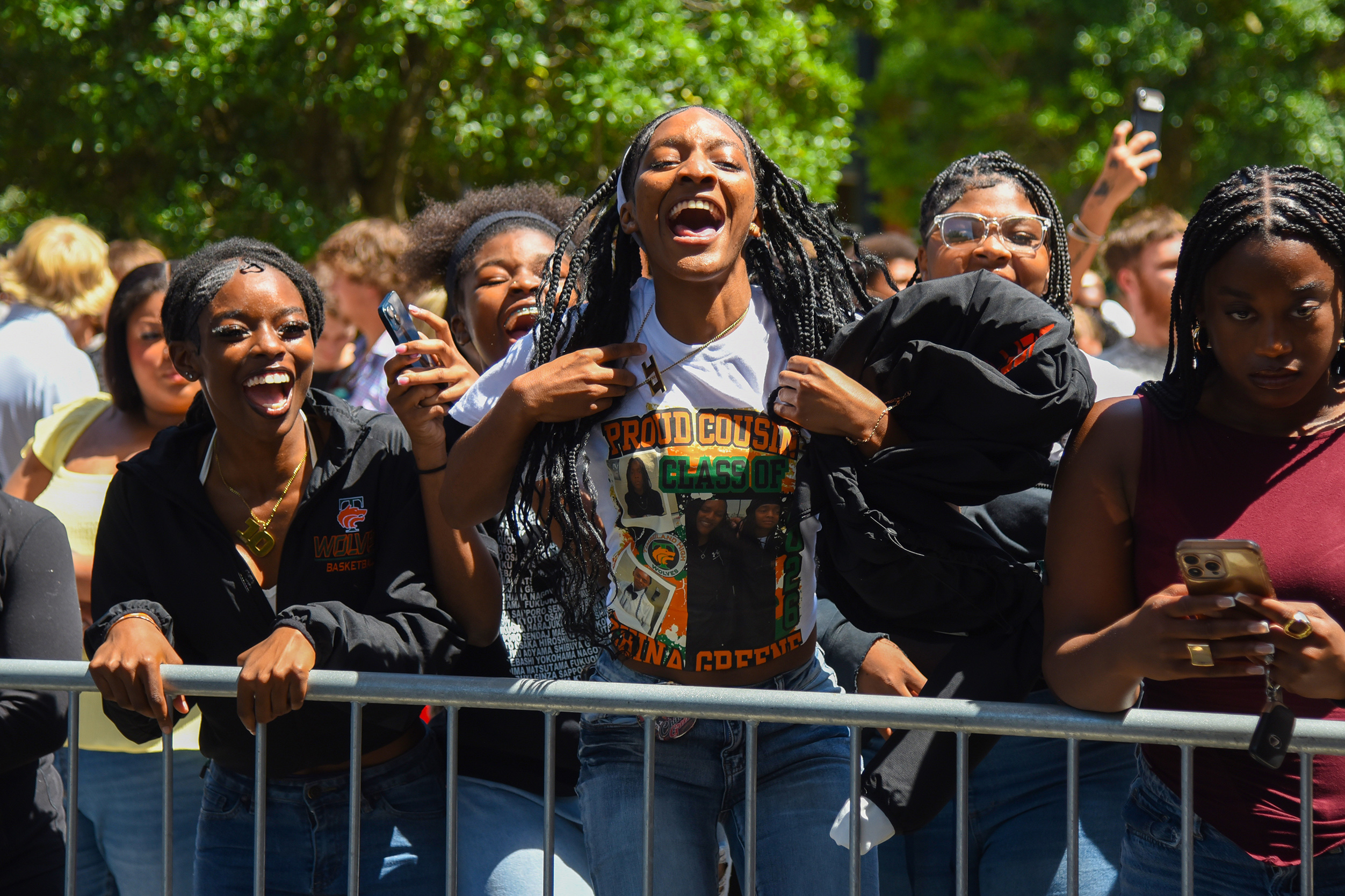 A group of people cheer and smile in an outdoor setting with trees and a metal barrier.