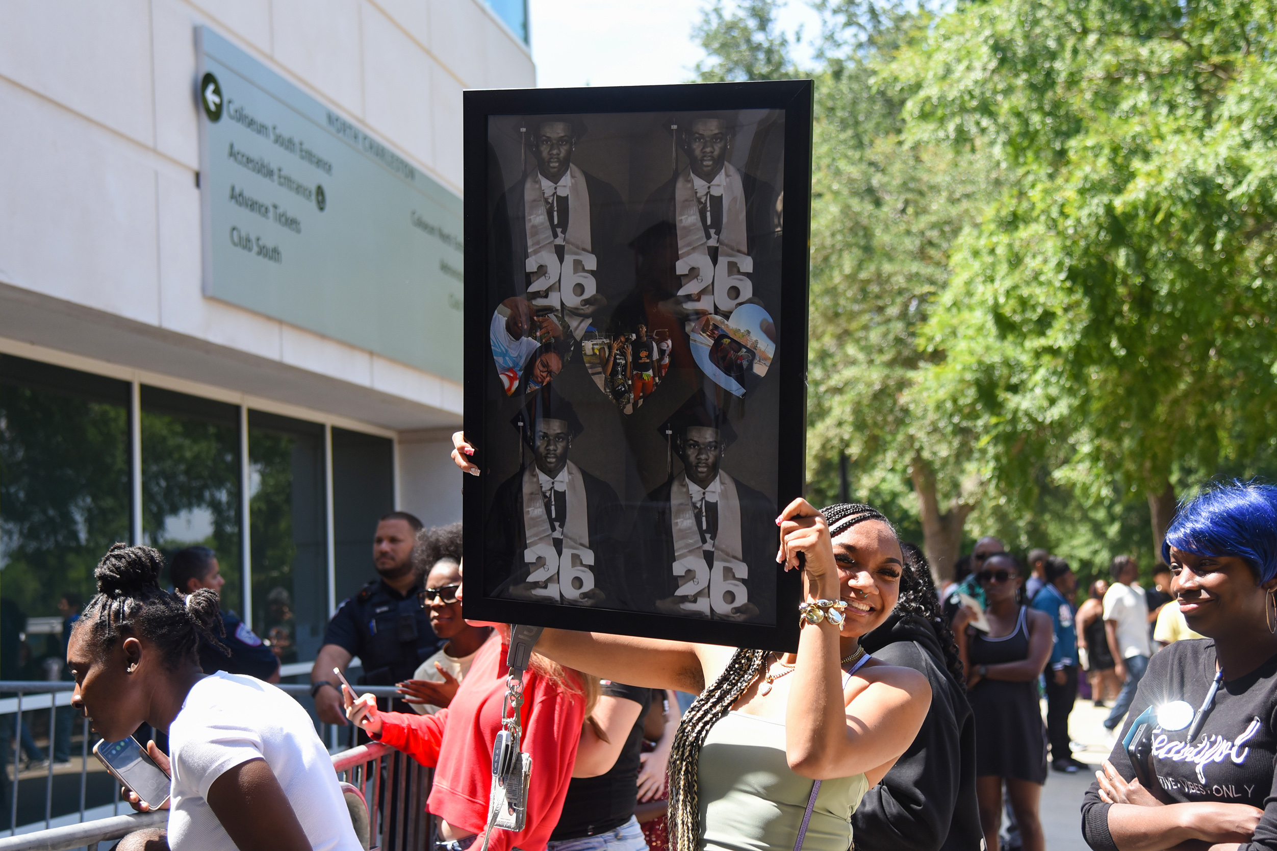 A person holds a framed picture of three men with numbers in front of a crowd.