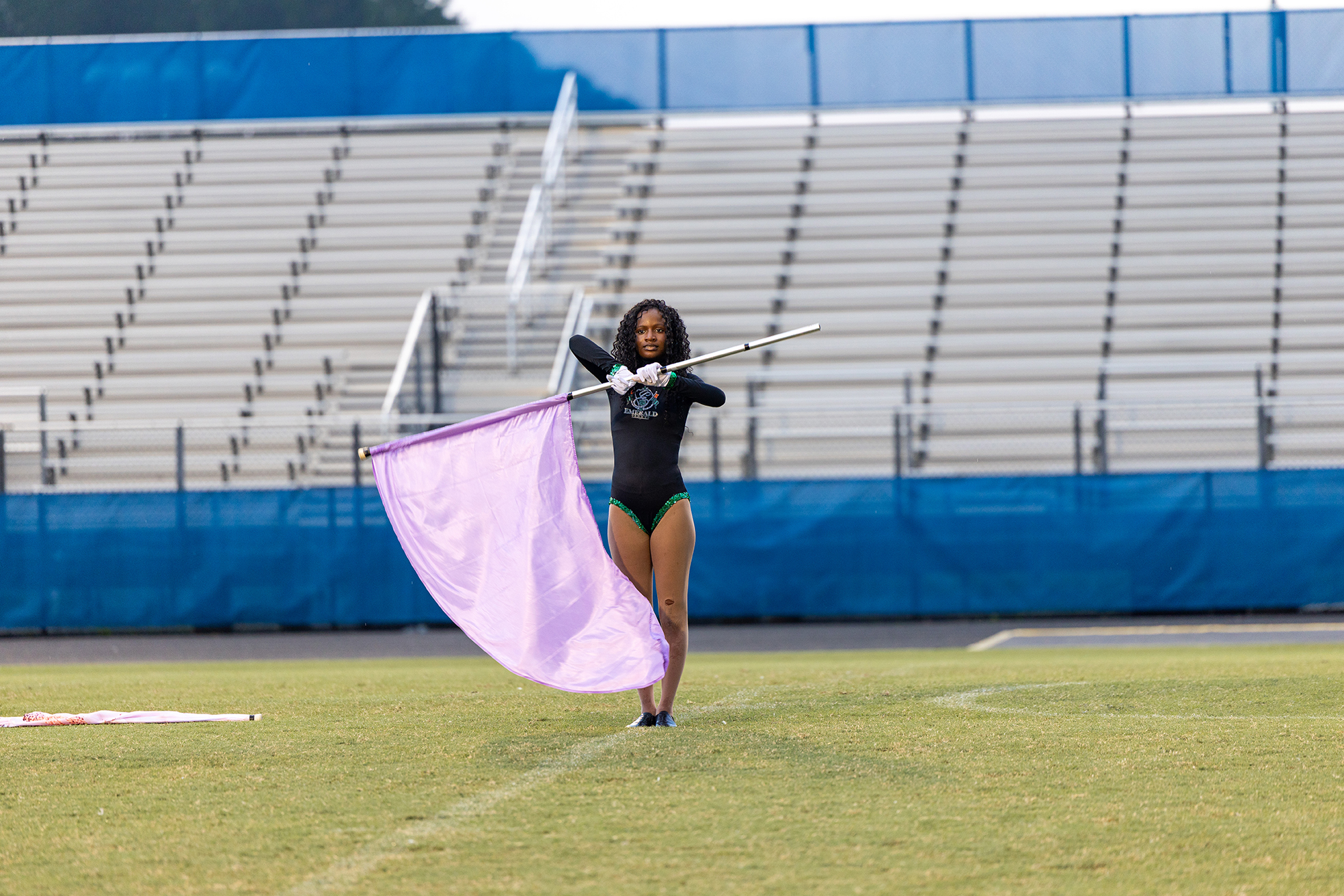 A person with a purple flag stands on a field with empty bleachers behind them.
