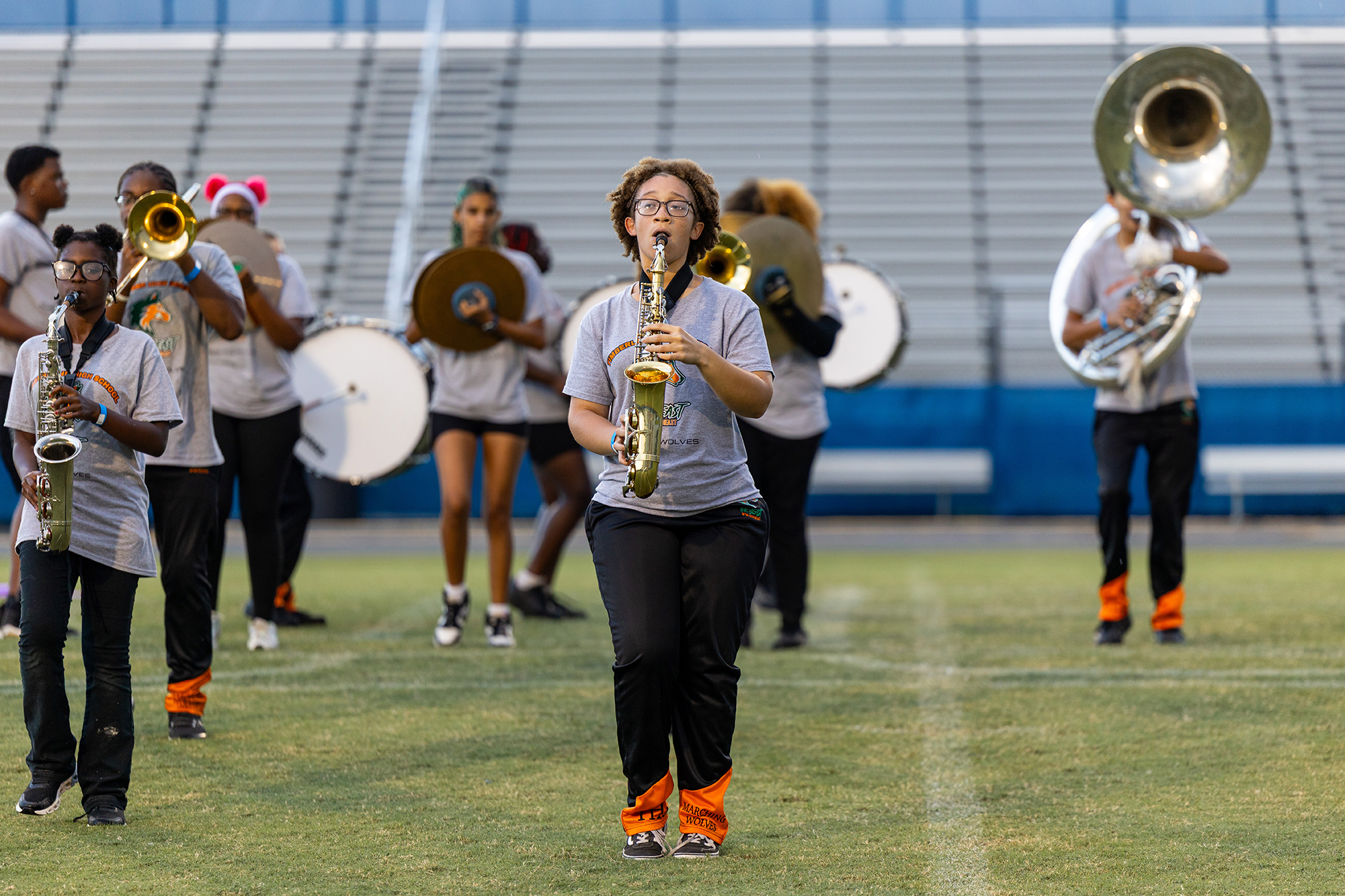 A group of individuals playing various musical instruments on a field with bleachers in the background.