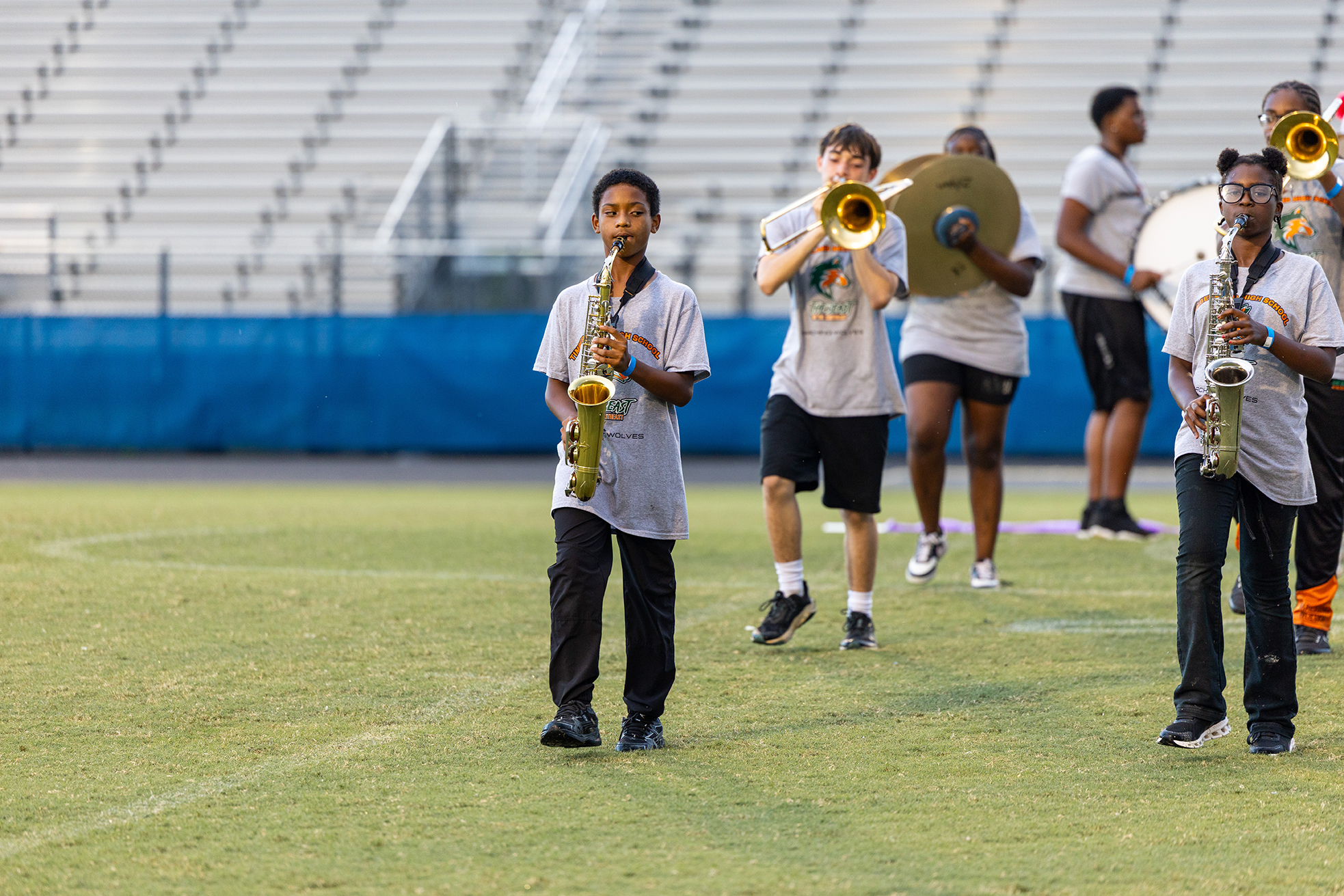 A group of young people dressed in matching gray shirts and black pants play instruments on a field.