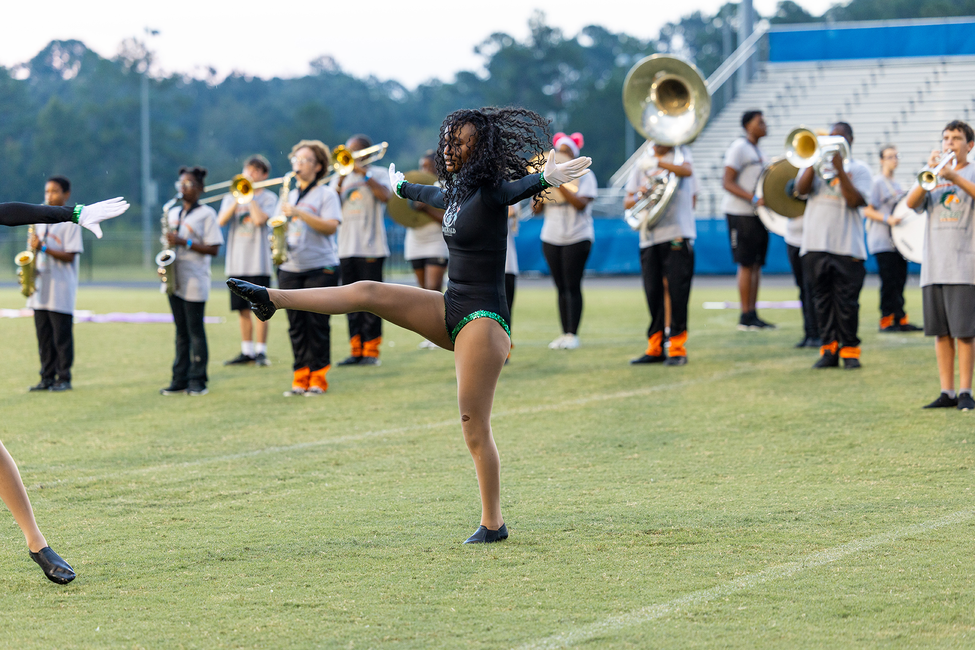 A person doing a split on a field. Behind them are several people playing instruments and standing on the field.