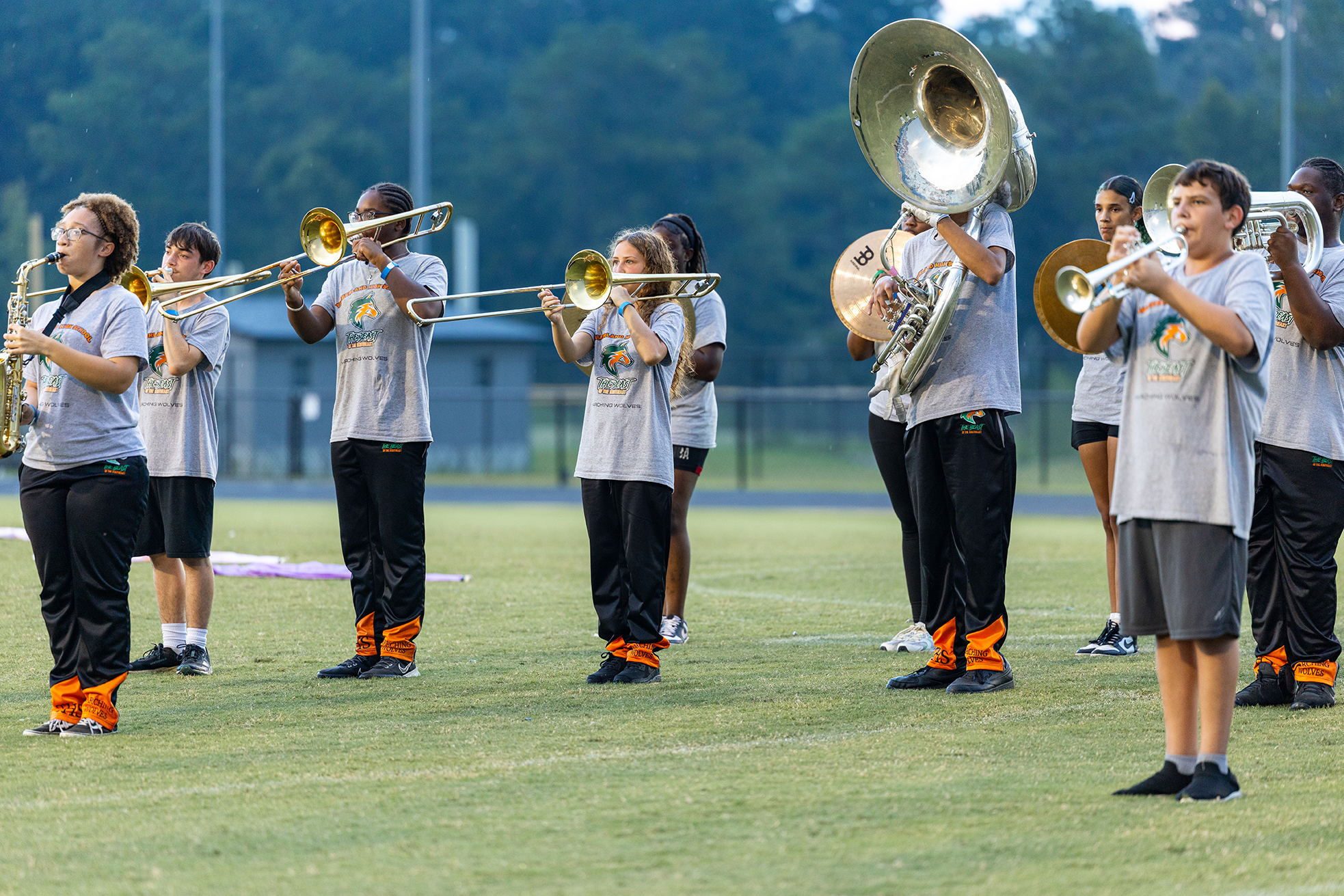 People in matching uniforms stand in a line on a field, playing various musical instruments.