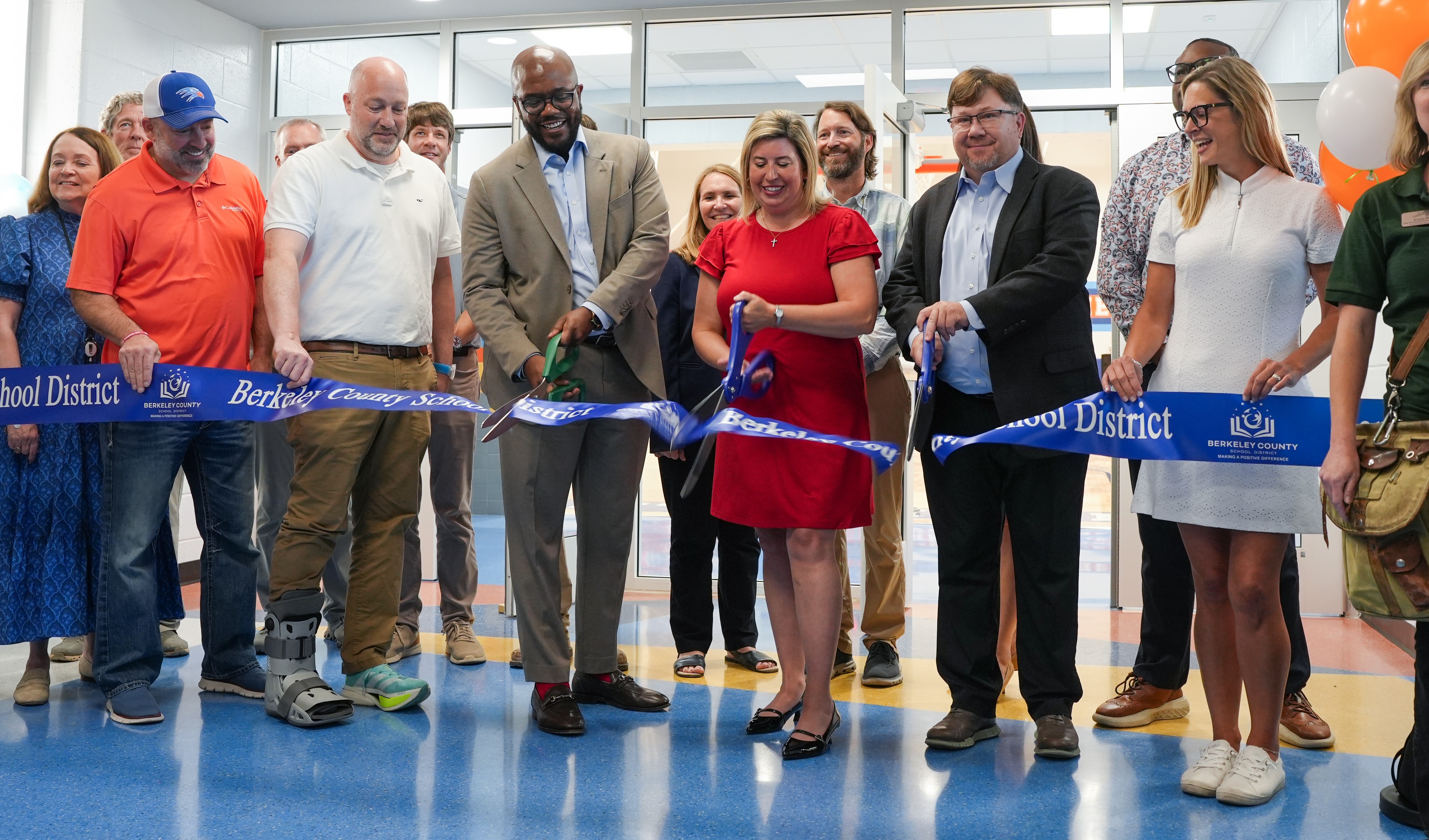 A group of people stand around a blue ribbon, holding scissors, and smiling. They are likely at a ribbon-cutting ceremony.