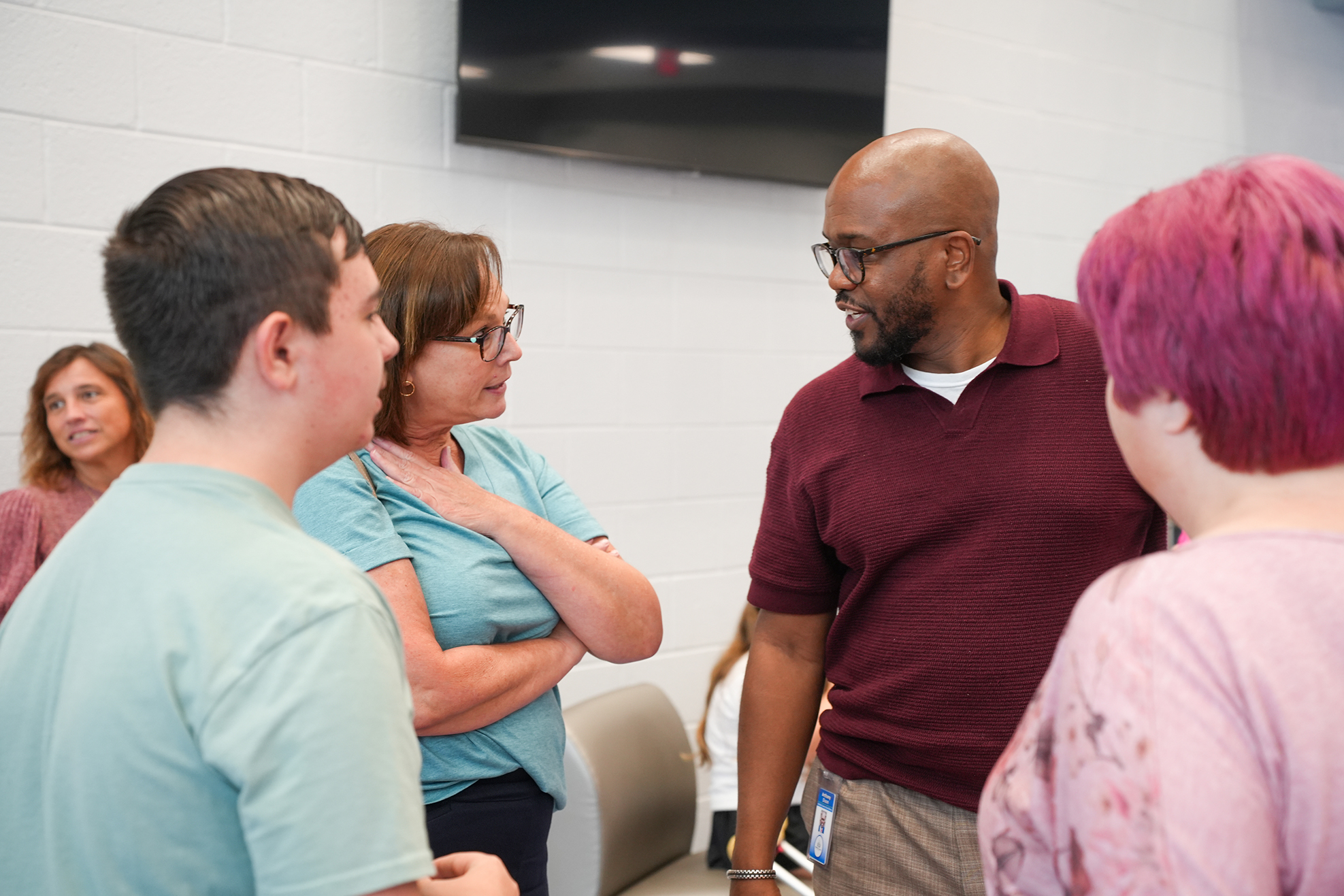 A group of people are in a room. They are engaged in conversation. Two women and two men are looking at each other.