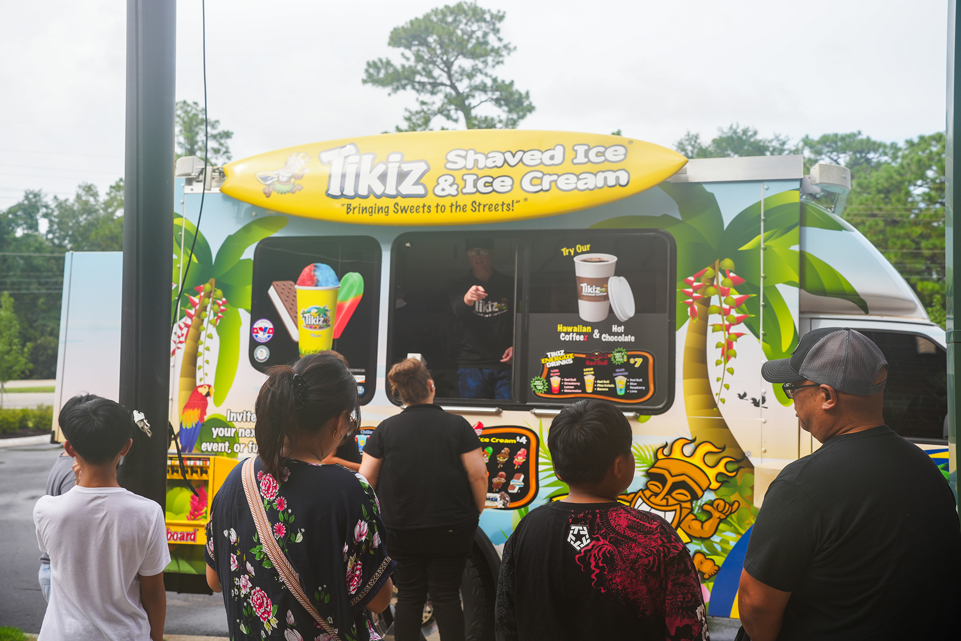 A shaved ice truck with a tropical theme. People are gathered in front of it.