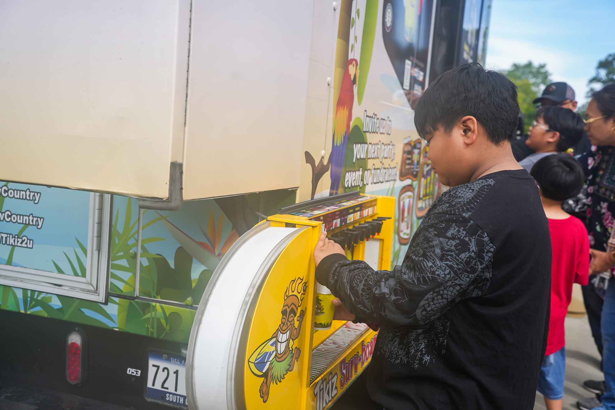 A boy in black holds a yellow container at a food truck with a colorful mural.