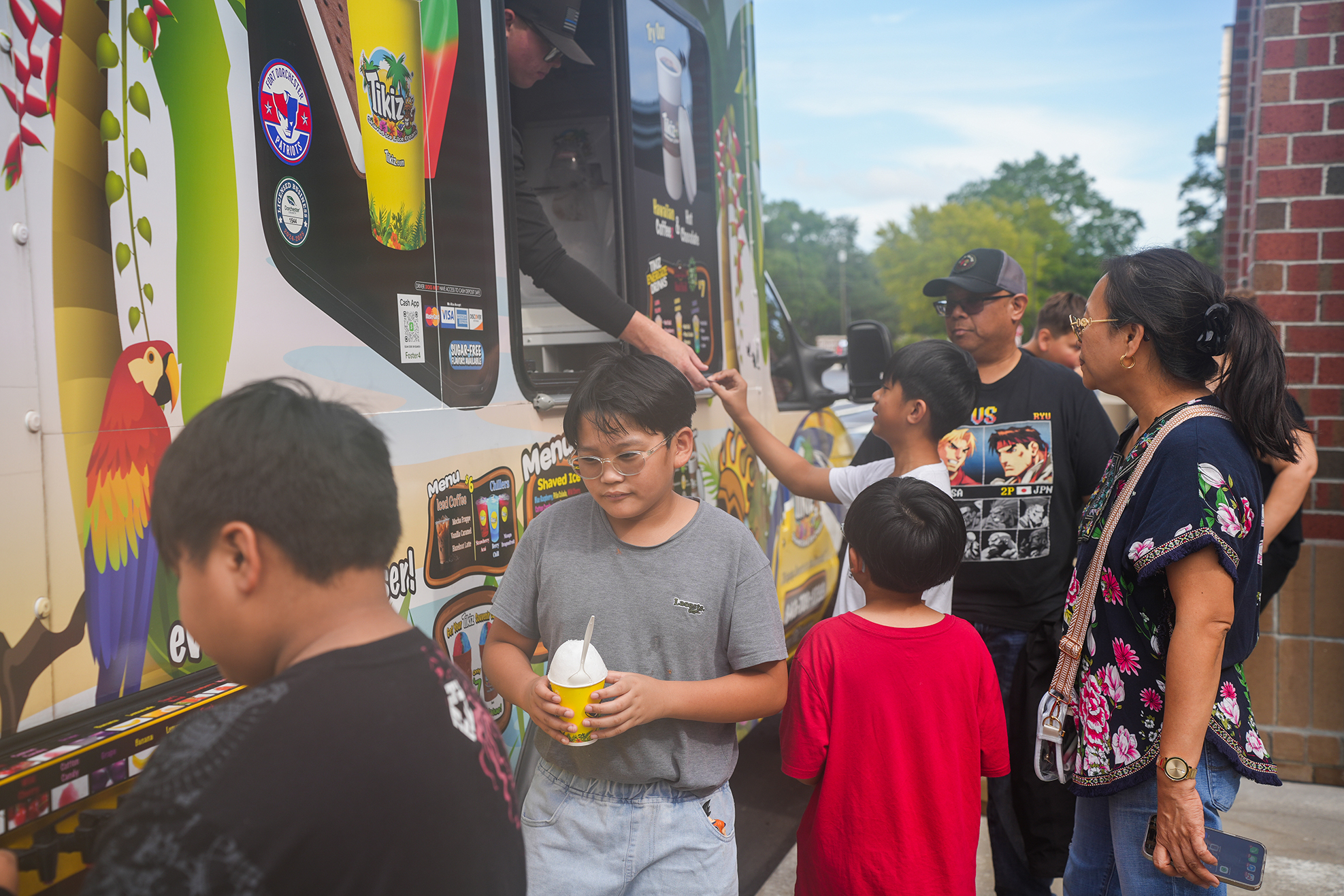 A group of people, including children, stand around an ice cream truck with colorful graphics.