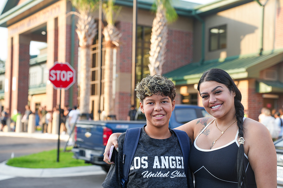 Two people standing outside a building with a blue pickup truck parked behind them. One wears a black "Los Angeles" shirt; the other wears a black top.
