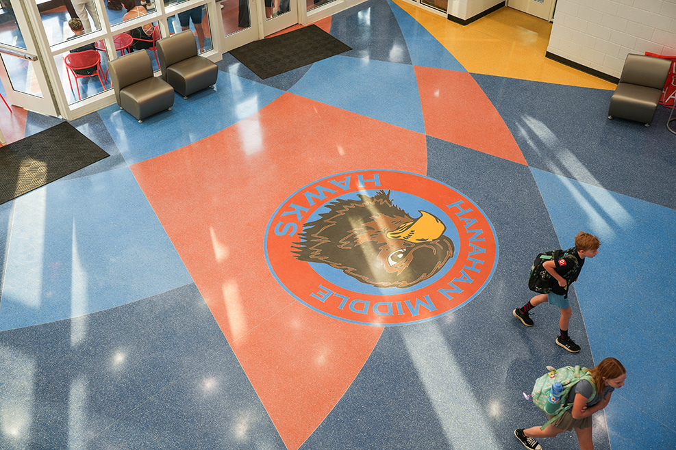 Overhead view of a school hallway. Two students walk by an orange and blue floor design.