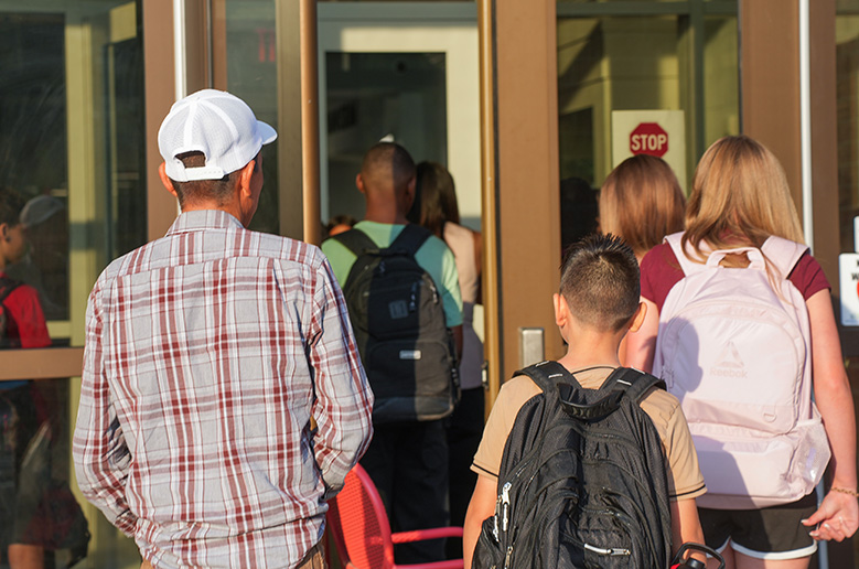People exiting a building. A man and a boy with backpacks in front, and two girls behind them.