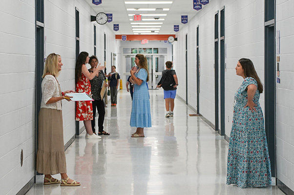 A hallway with people conversing in small groups; two women face each other in front of a wall.