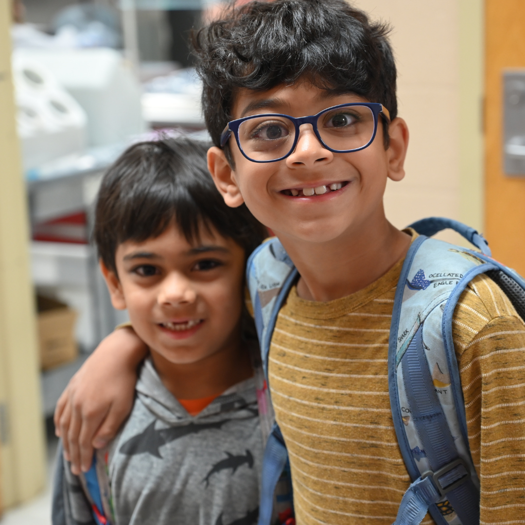 Two brothers, one with their arm around their shoulder, both smiling at the camera.