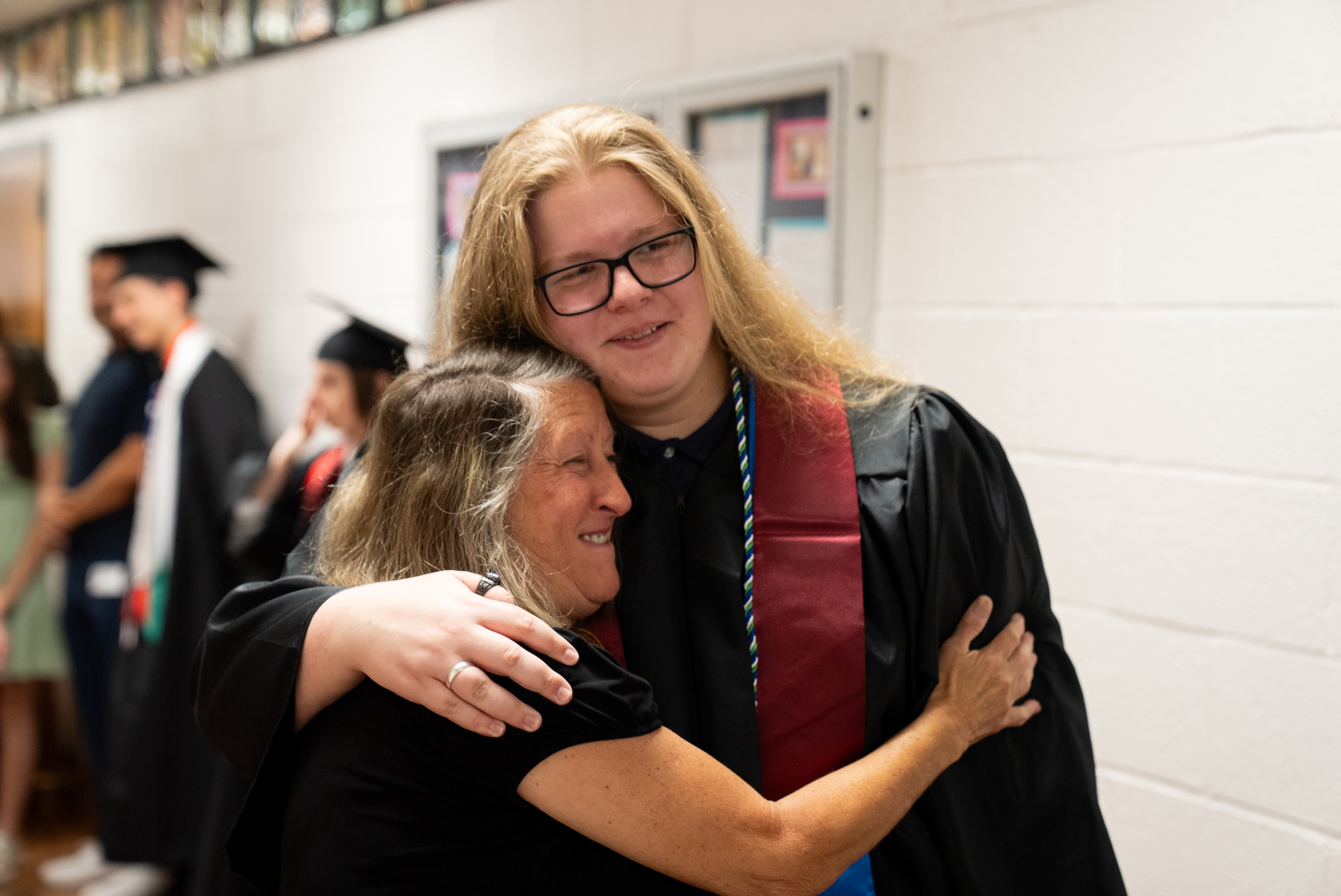 Two women hugging, one in a black gown and glasses, the other in a black shirt.