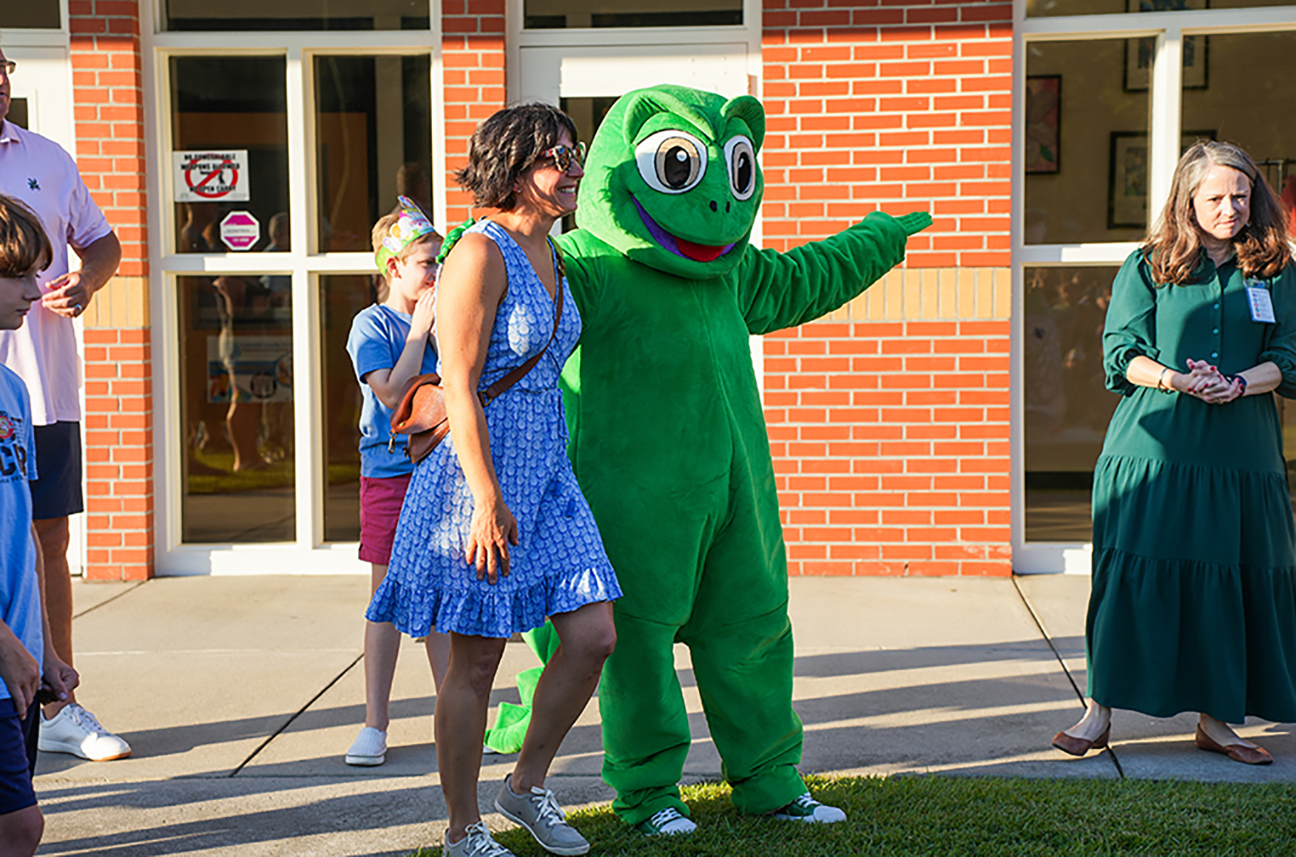 A group gathers on a sidewalk, with a woman in a green costume and another woman in green dress standing.