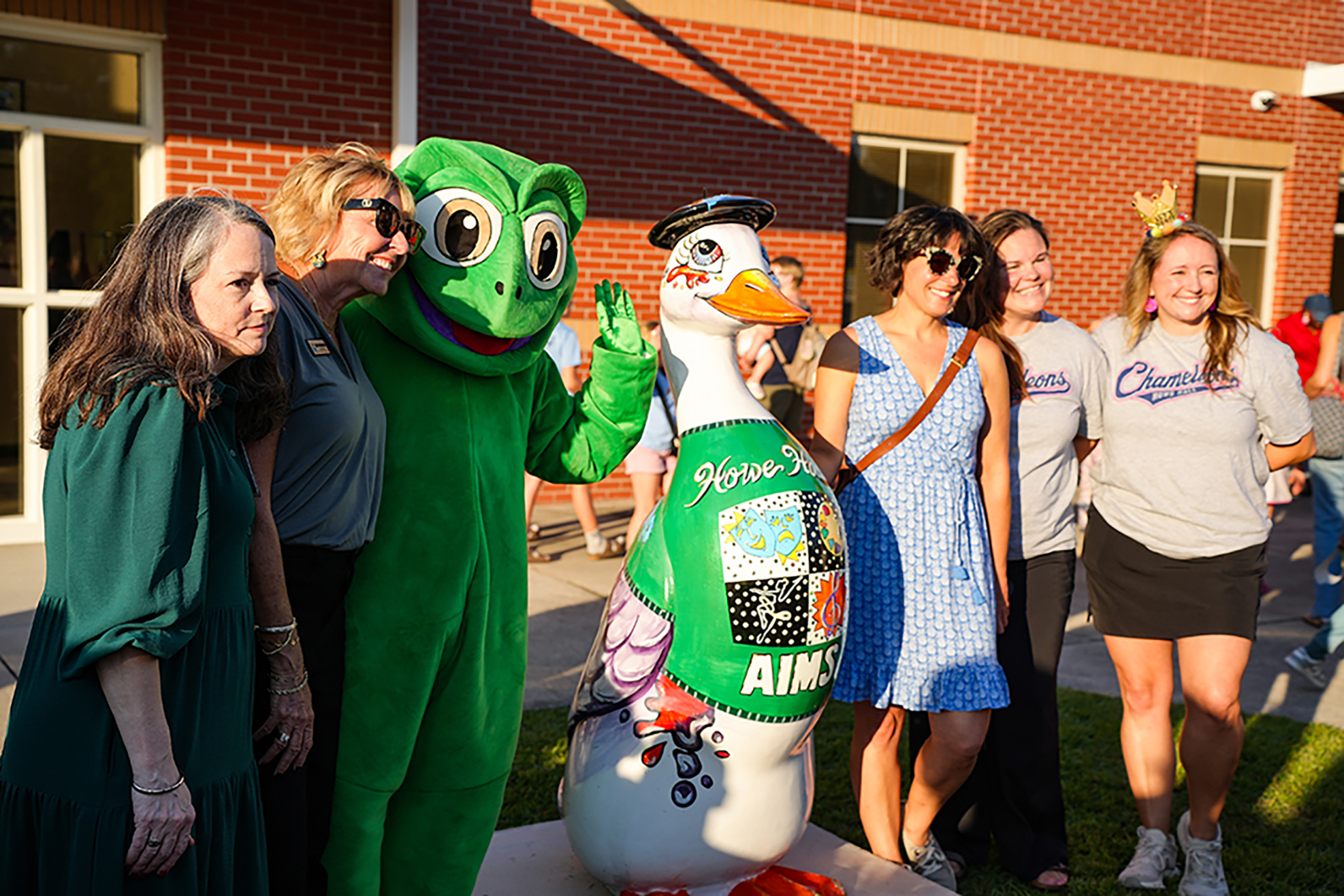 Five people pose for a photo with a mascot. The mascot is a large, green frog with a duck body.