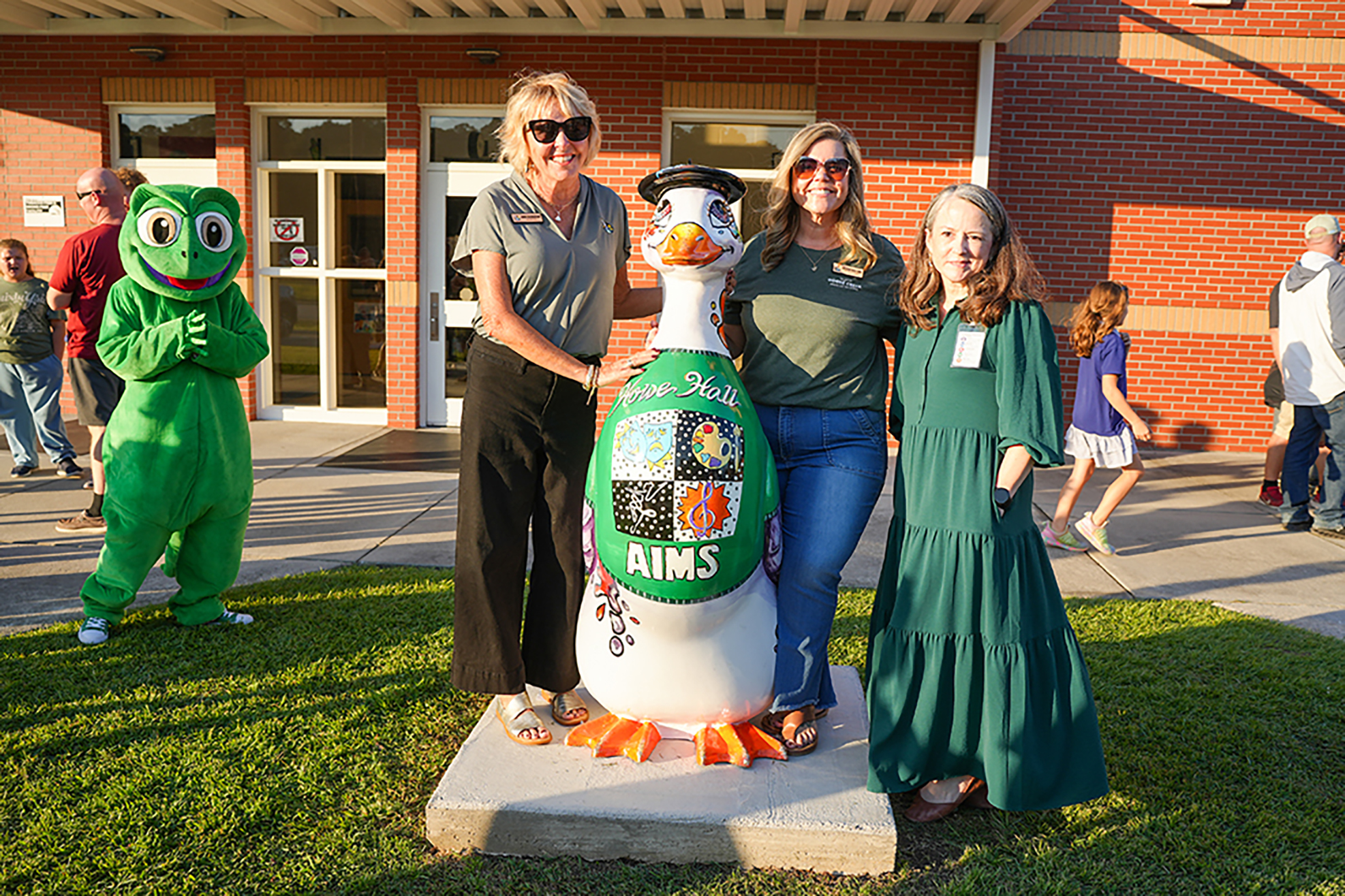 Four adults stand by a large penguin statue, two wearing green dresses, one in a grey shirt, and another in green.