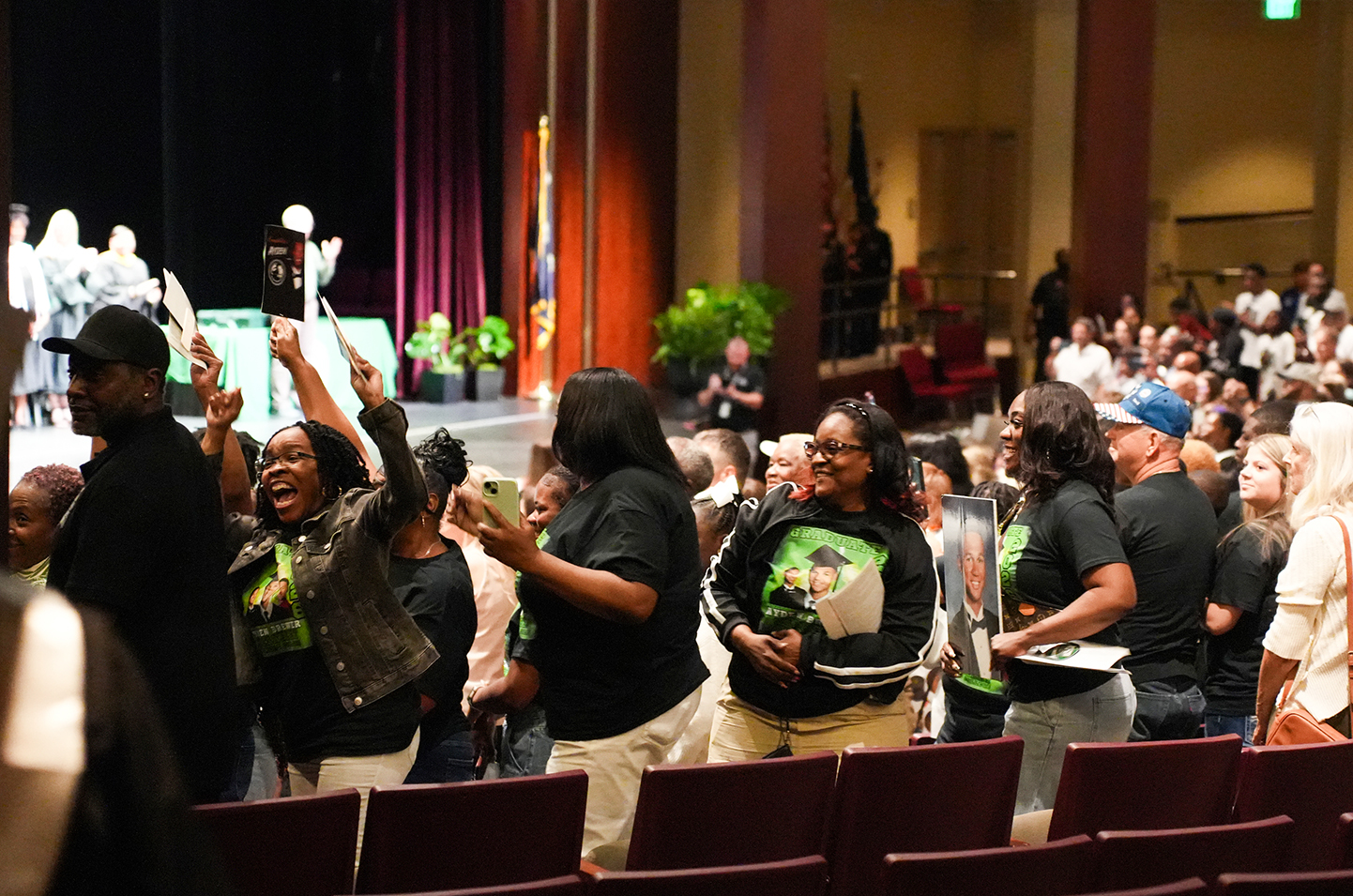 An audience of people wearing black shirts, standing and cheering in an auditorium.