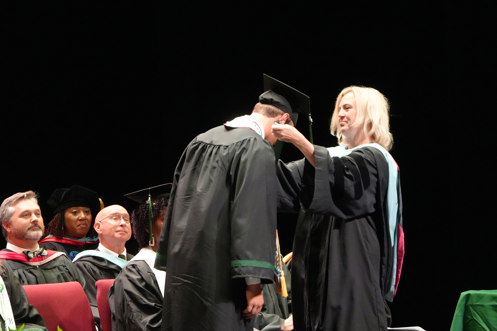 A person in a cap and gown is receiving an award from a woman in a gown.