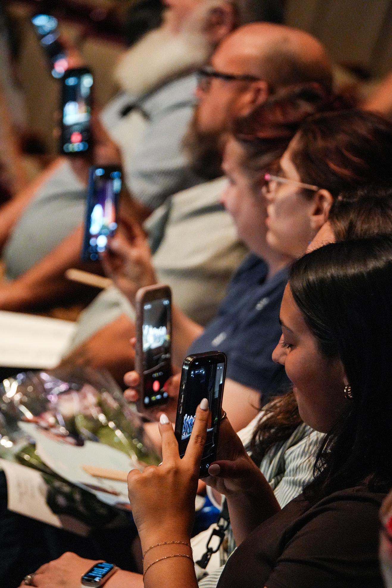 Several people are holding phones. They are seated in a row. One woman is using a phone.
