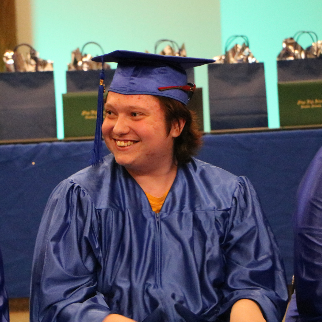 Student smiling at the crowd at graduation sitting in cap and gown