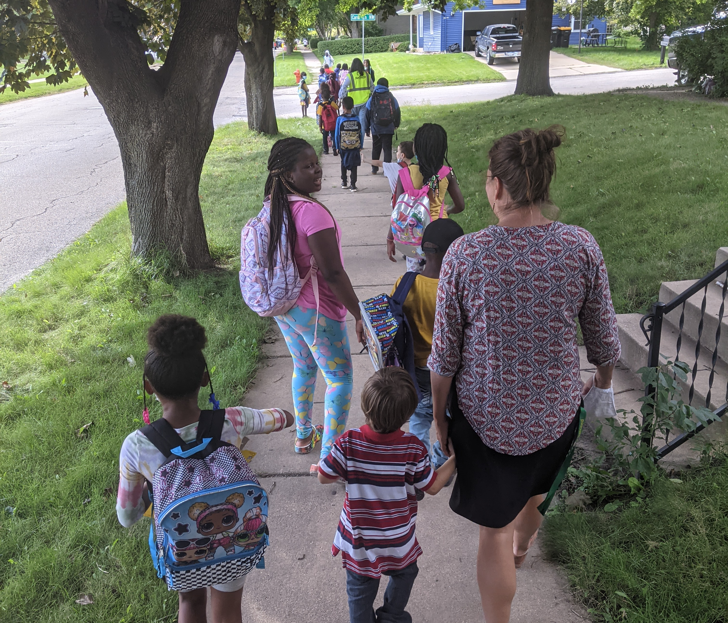 A child is holding an adult's hand while walking down a sidewalk.