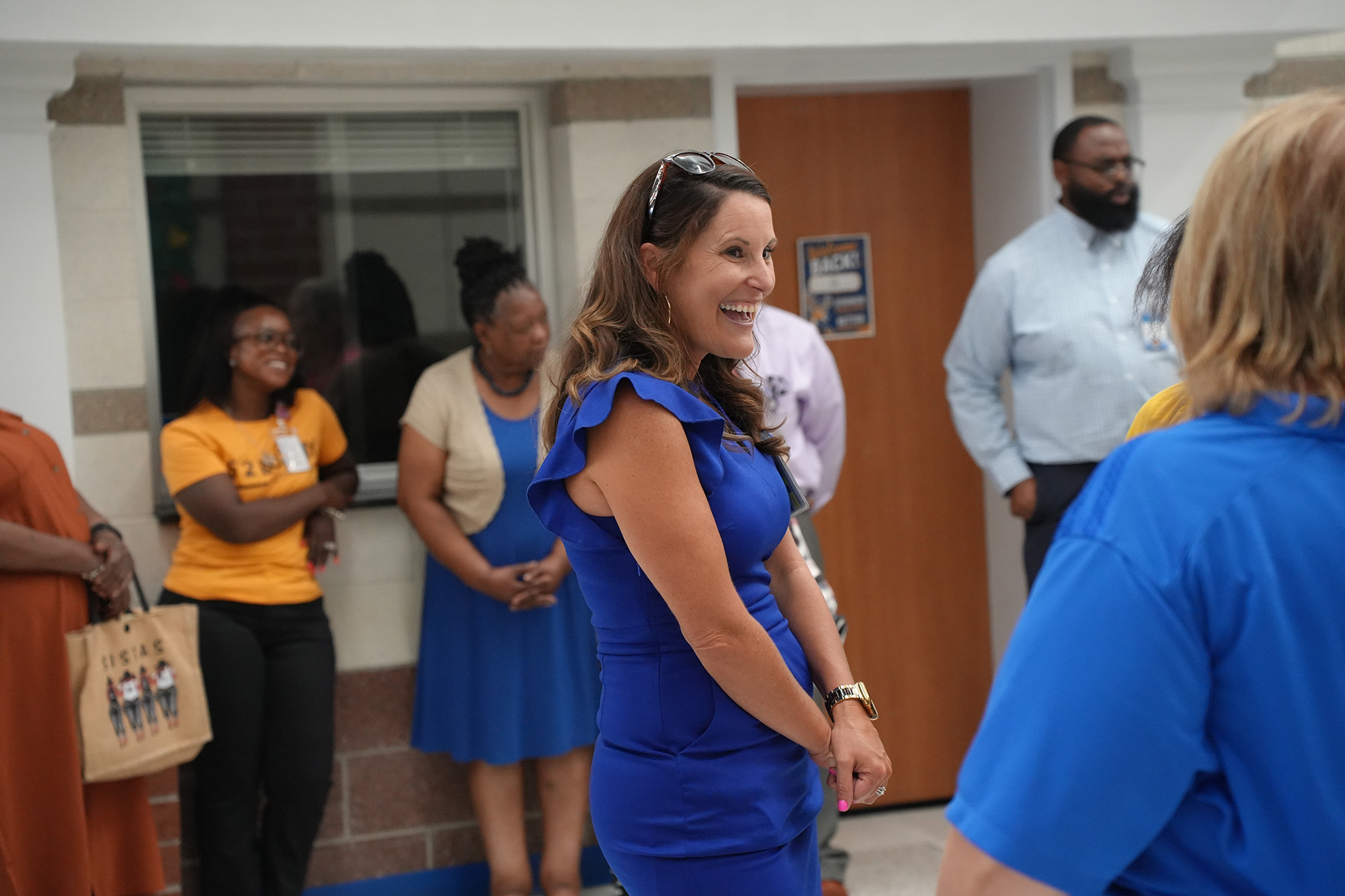 A woman in a blue dress converses with others, including a woman in blue and a man in white.