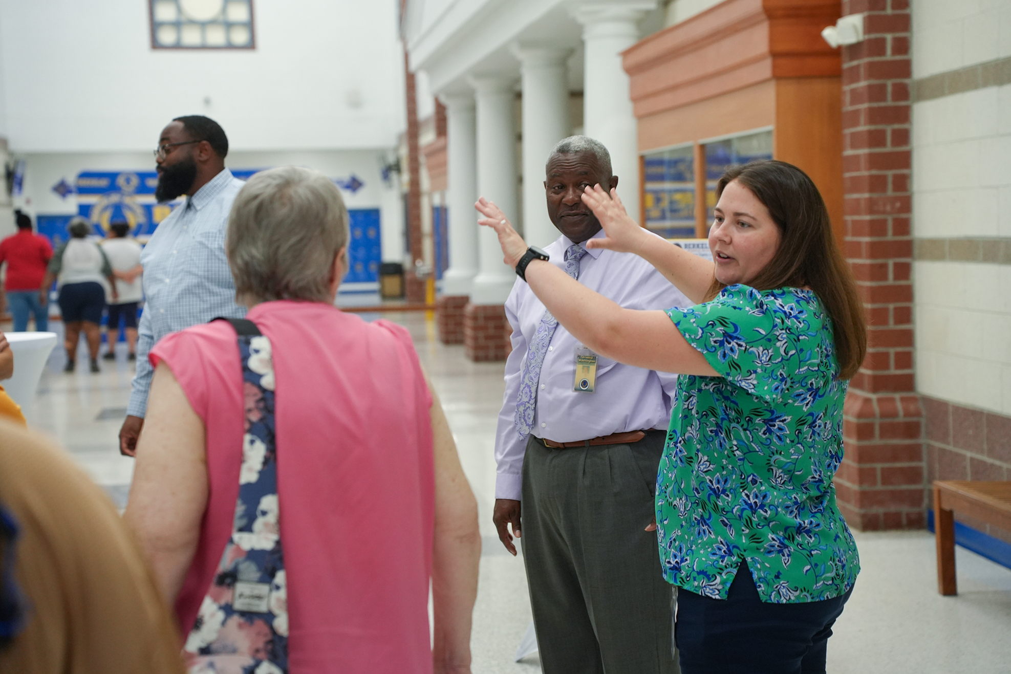 A woman with long dark hair speaks to a man in a light blue shirt while gesturing.