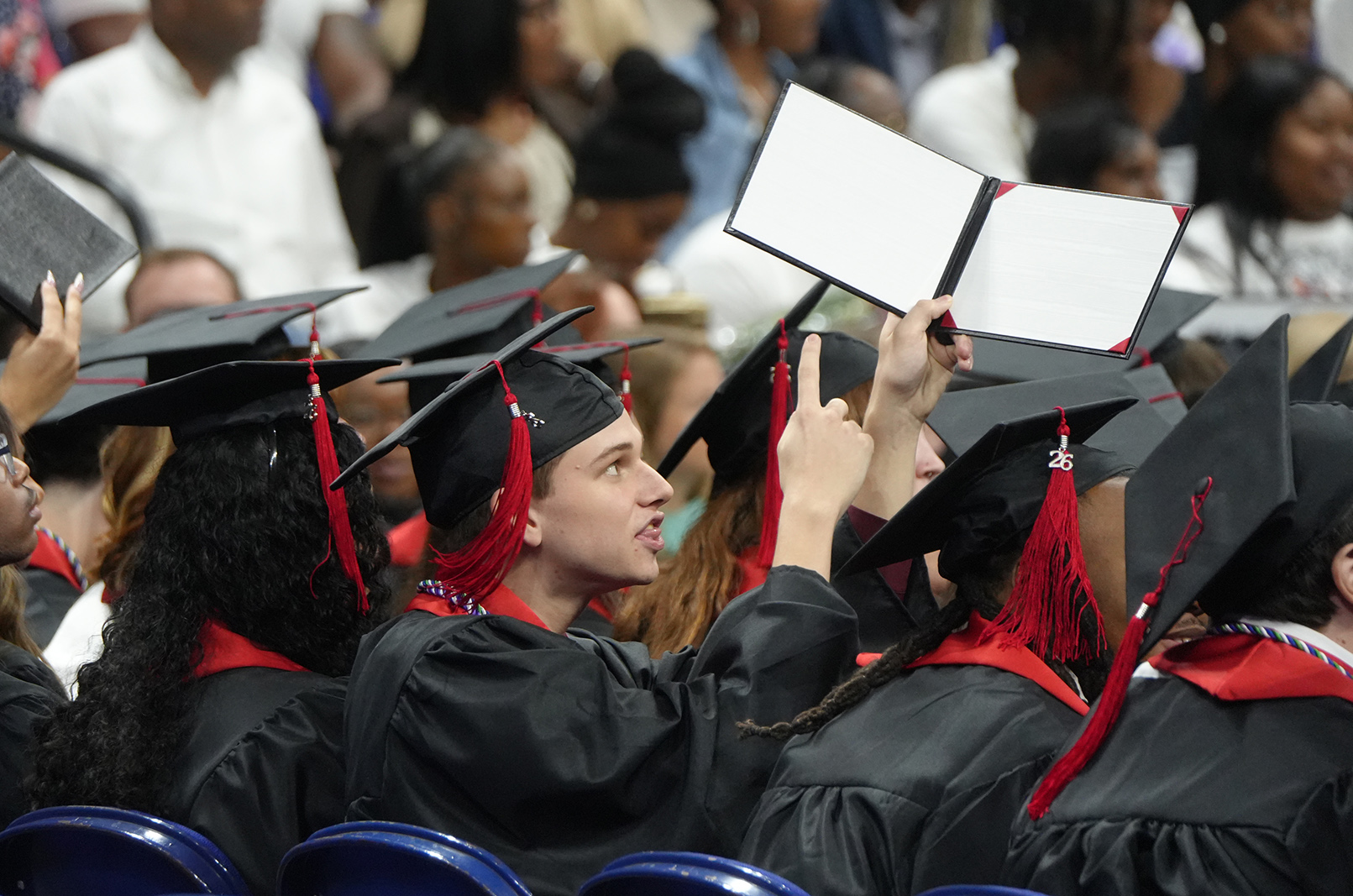 A group of people wearing black gowns and hats are attending a graduation ceremony, with one holding a diploma.