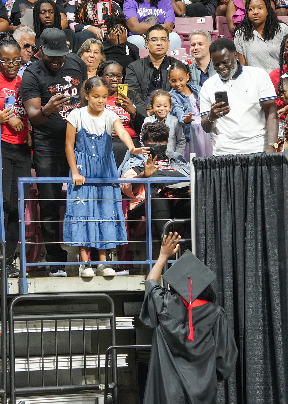A person in a cap and gown holds the hand of a girl in a dress at an event.