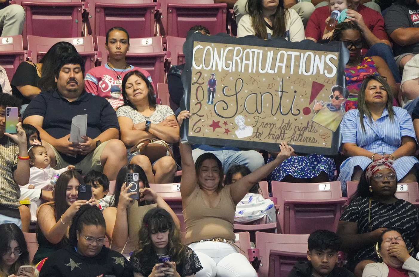 Audience members in a stadium hold up a sign that reads "Congratulations Santi" above their heads.