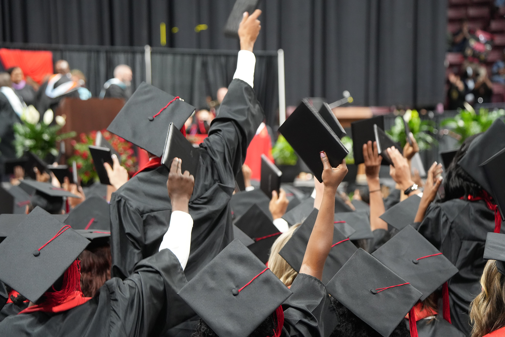 A group of people wearing black graduation gowns and caps celebrate at a ceremony.