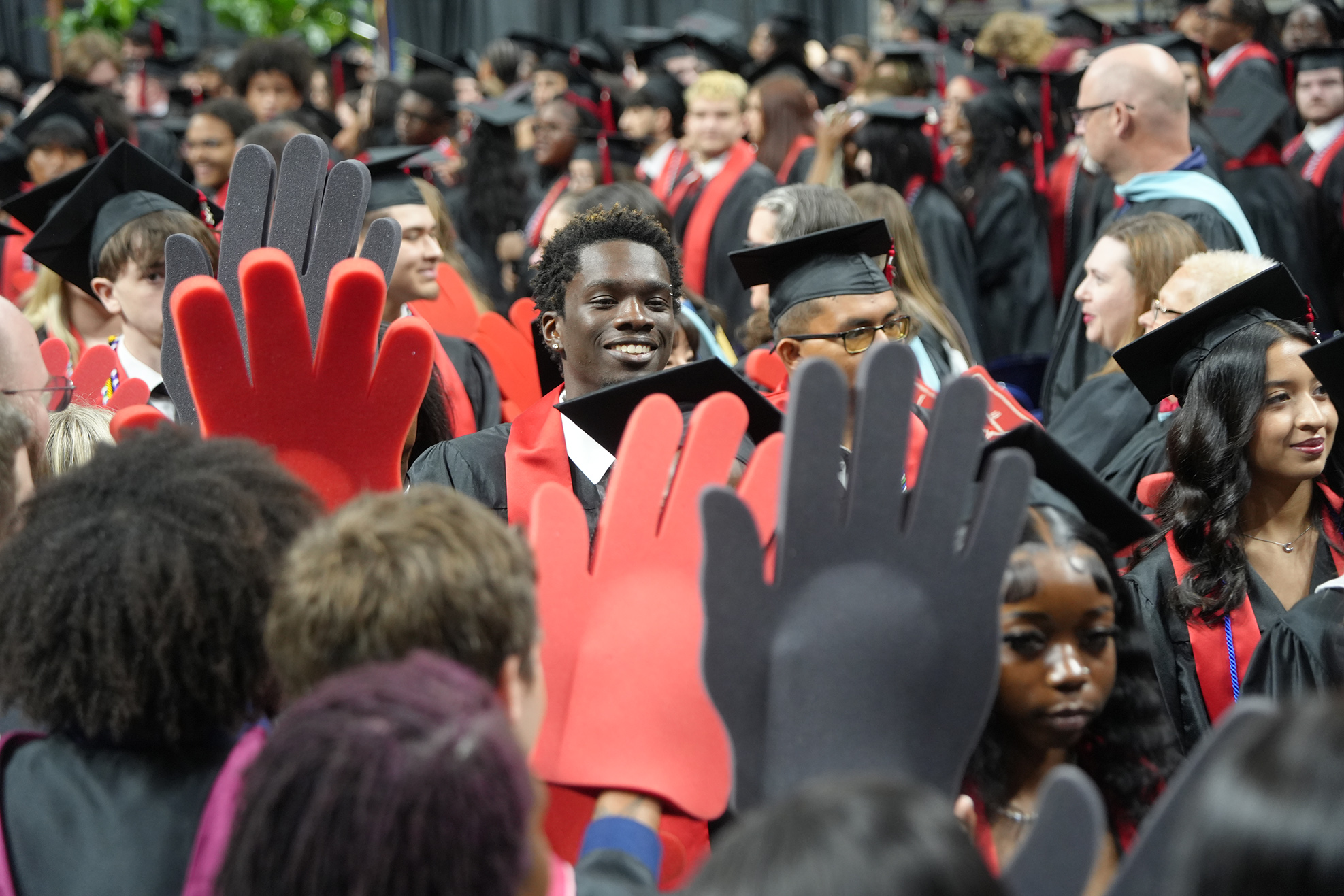 A large crowd of people in black and red graduation robes and hats; some wear red and black hand covers.