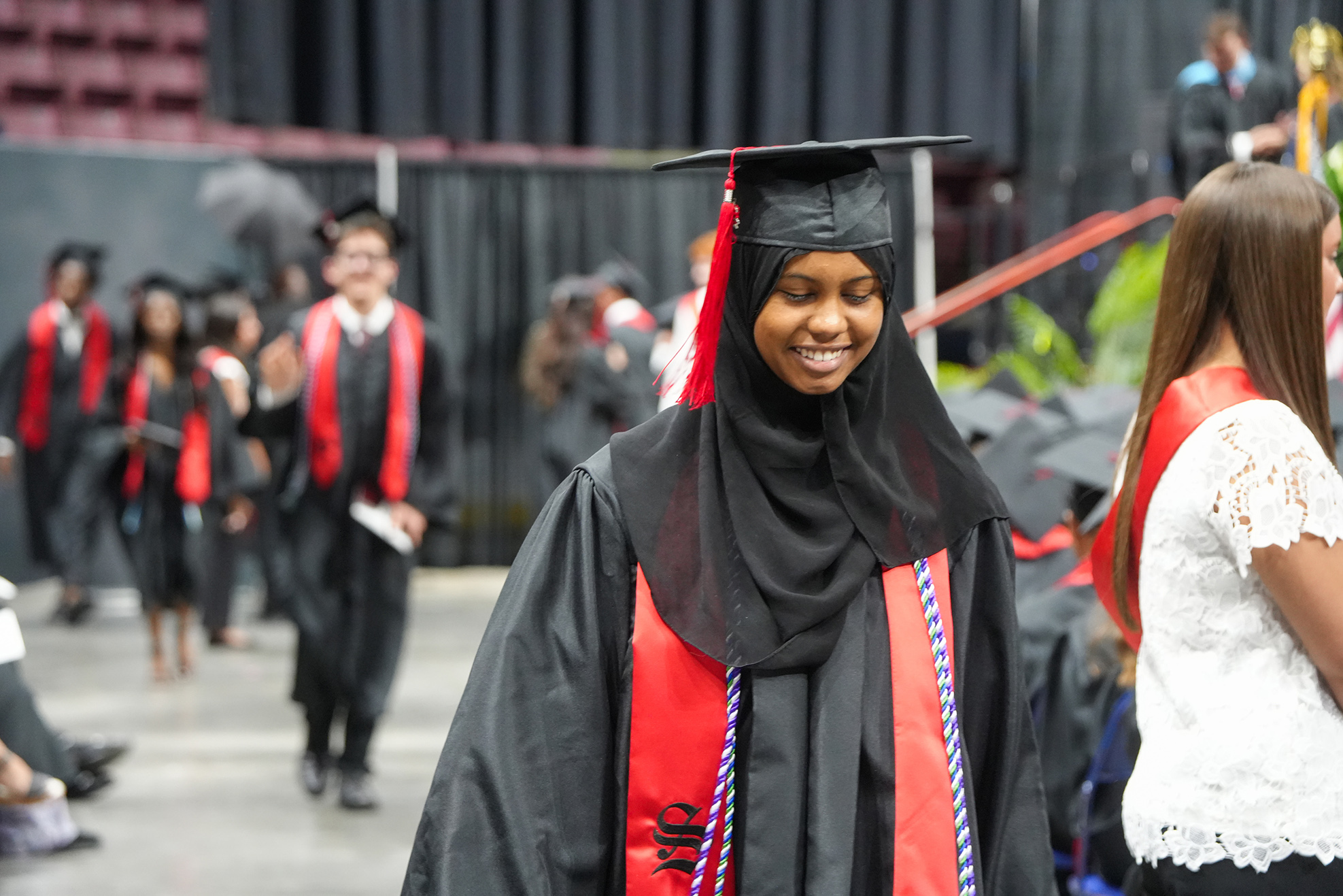 A woman in a black robe and graduation cap walks in a line with other graduates.