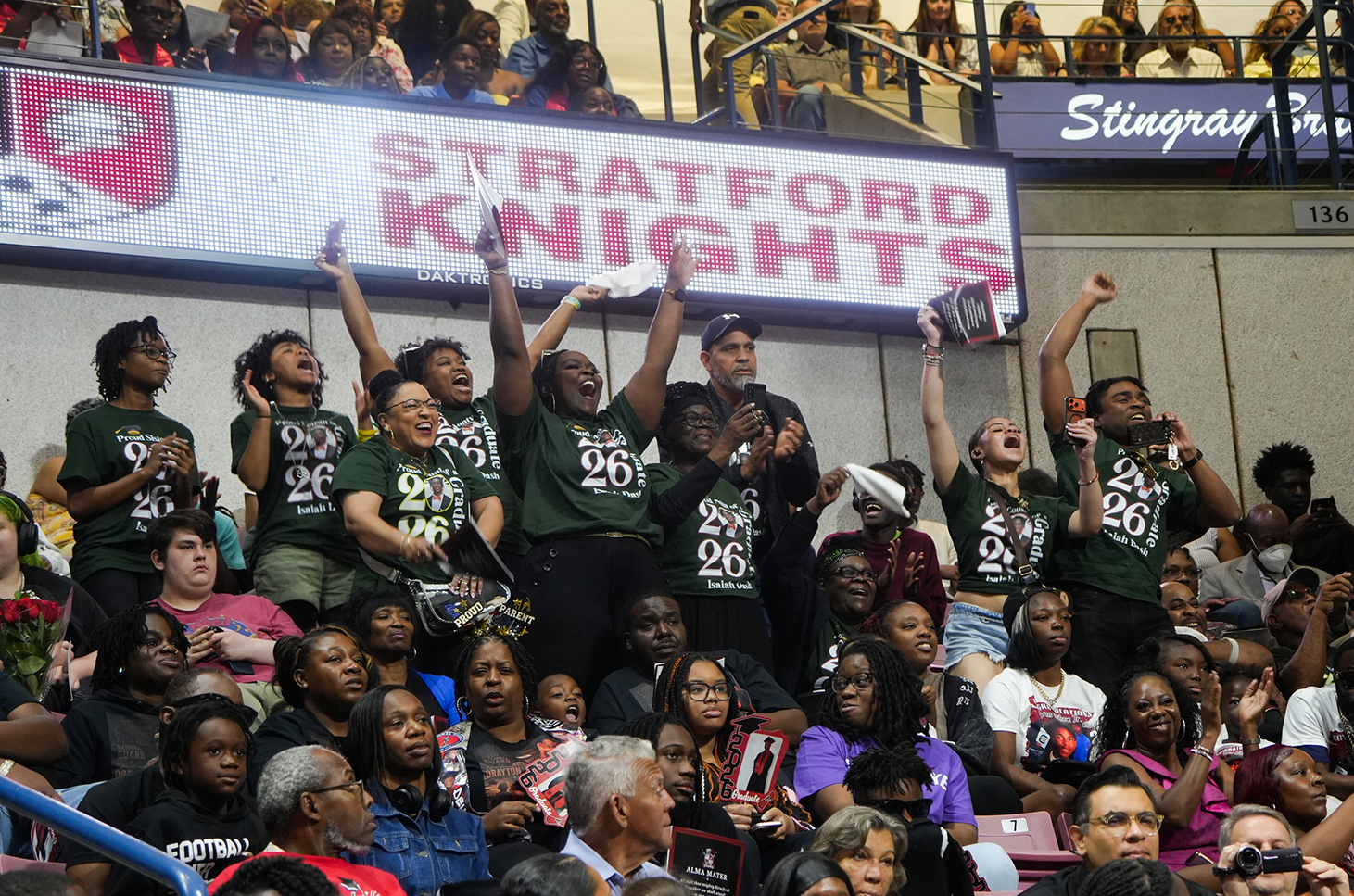Stadium audience in green shirts, cheering. Sign above reads "Stratford Knights." Stairs and spectators in the background.
