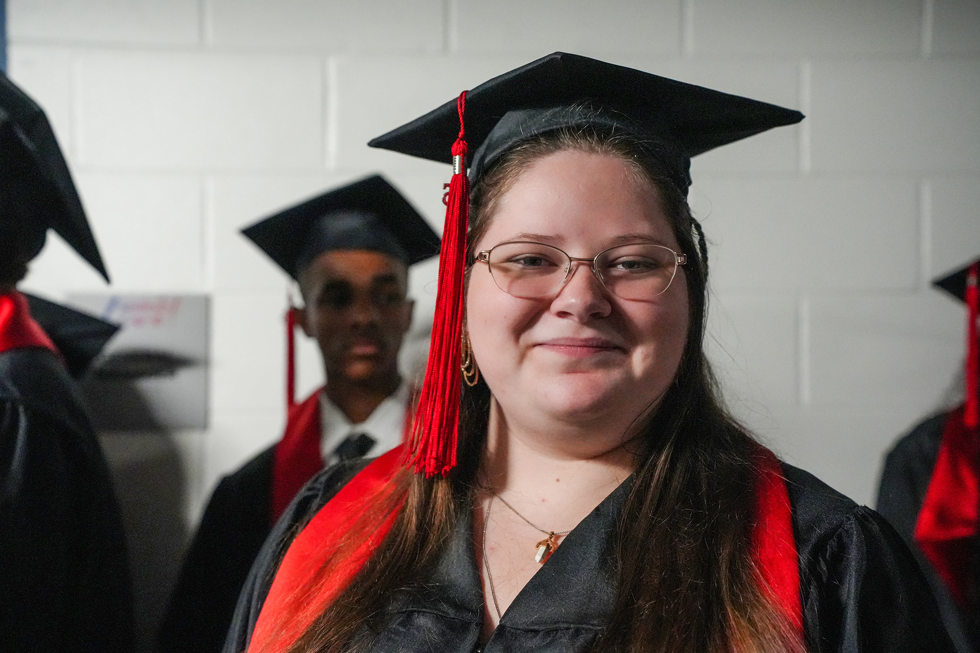 Woman in cap and gown stands with other graduates. She wears glasses and a necklace.