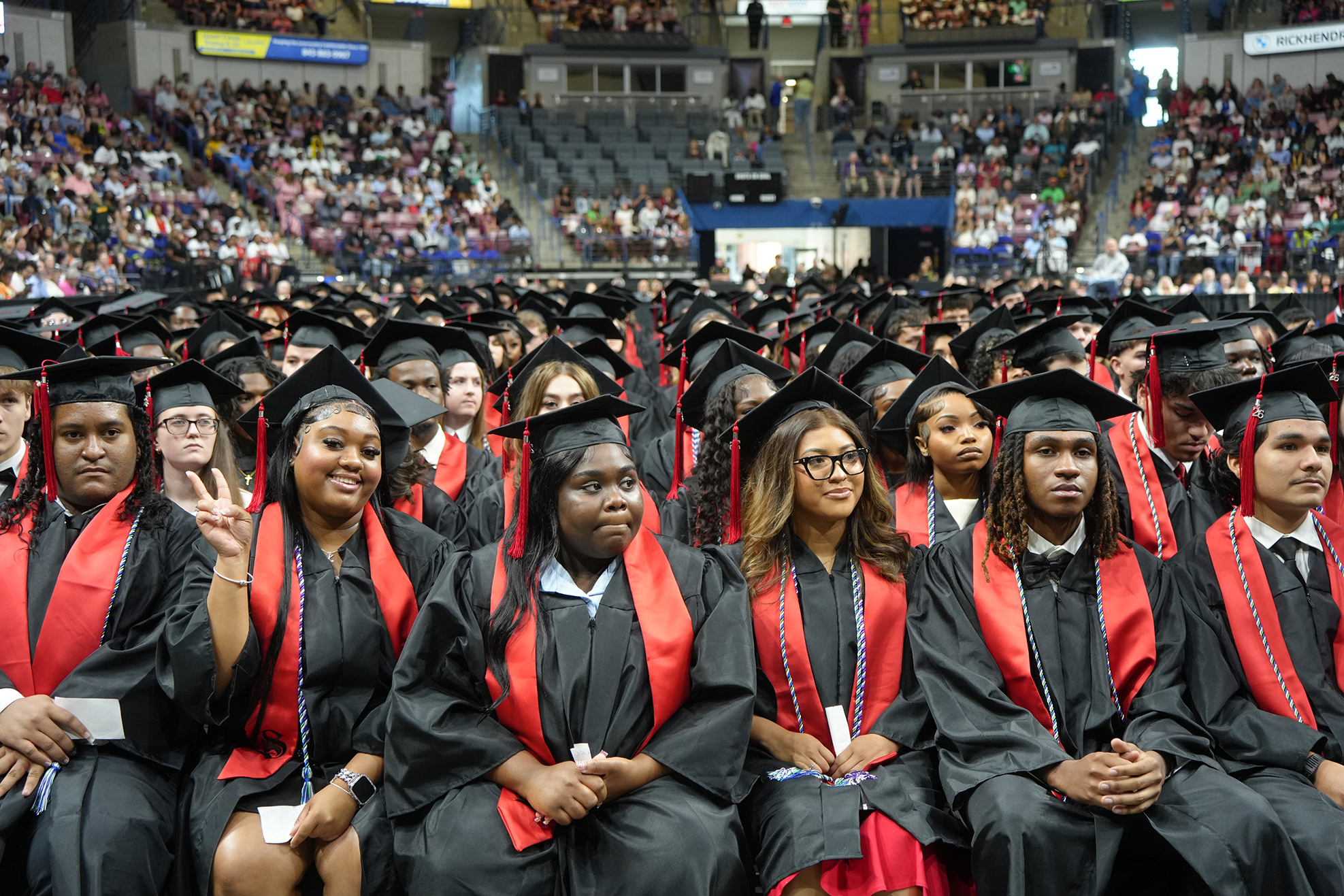 A large audience of people in red and black graduation gowns and caps, seated in rows.