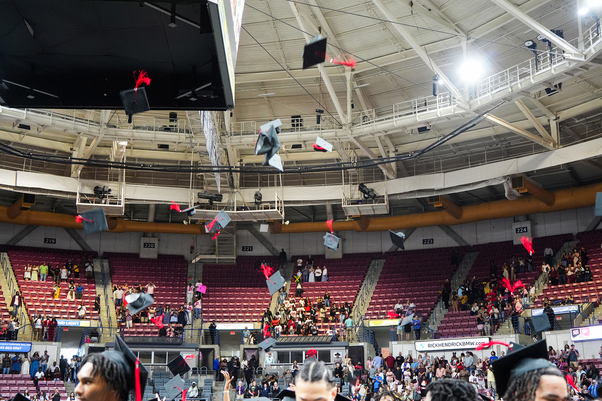 A stadium with a high ceiling. Many people are wearing graduation caps. Some are tossing them into the air.