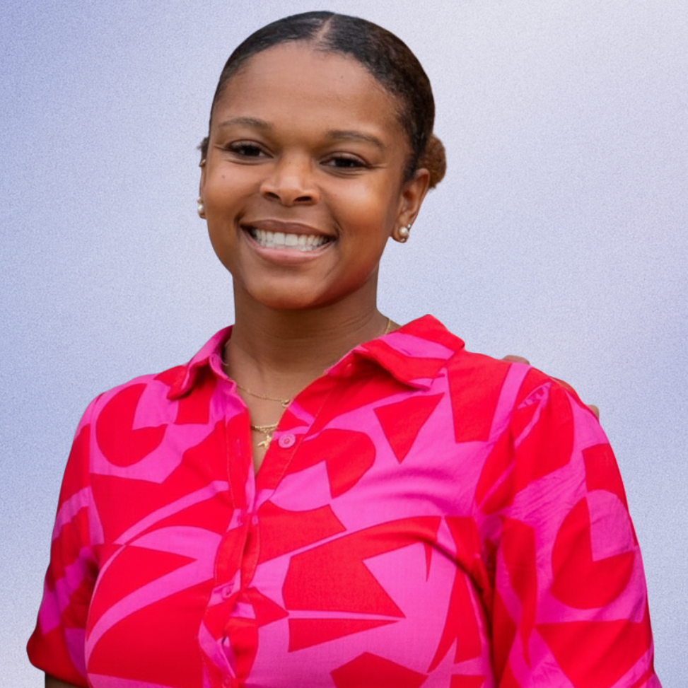 Person smiling, standing against a pink background. Wearing a pink, patterned shirt with a round collar.
