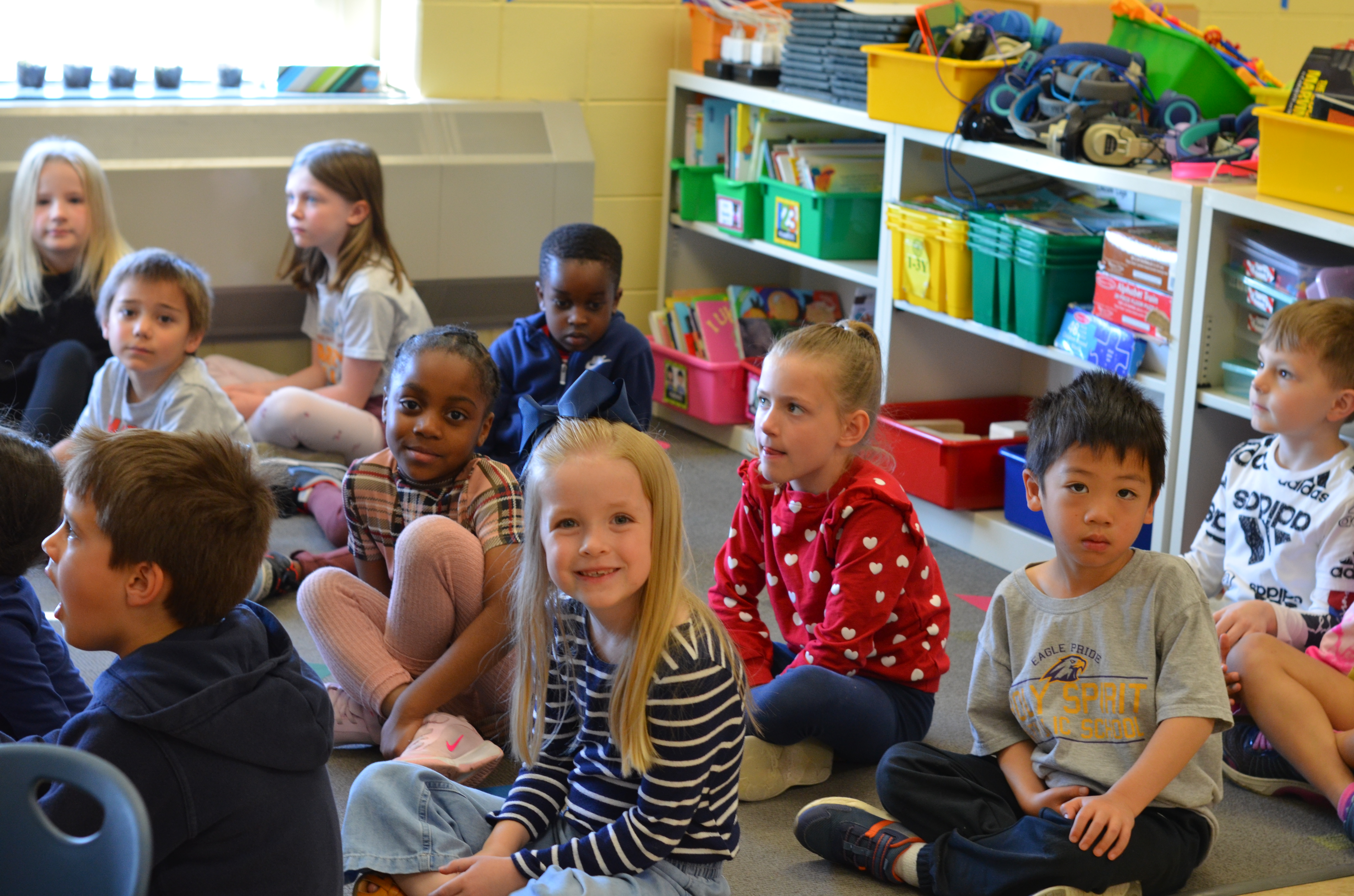 students sitting on carpet, smiling at camera