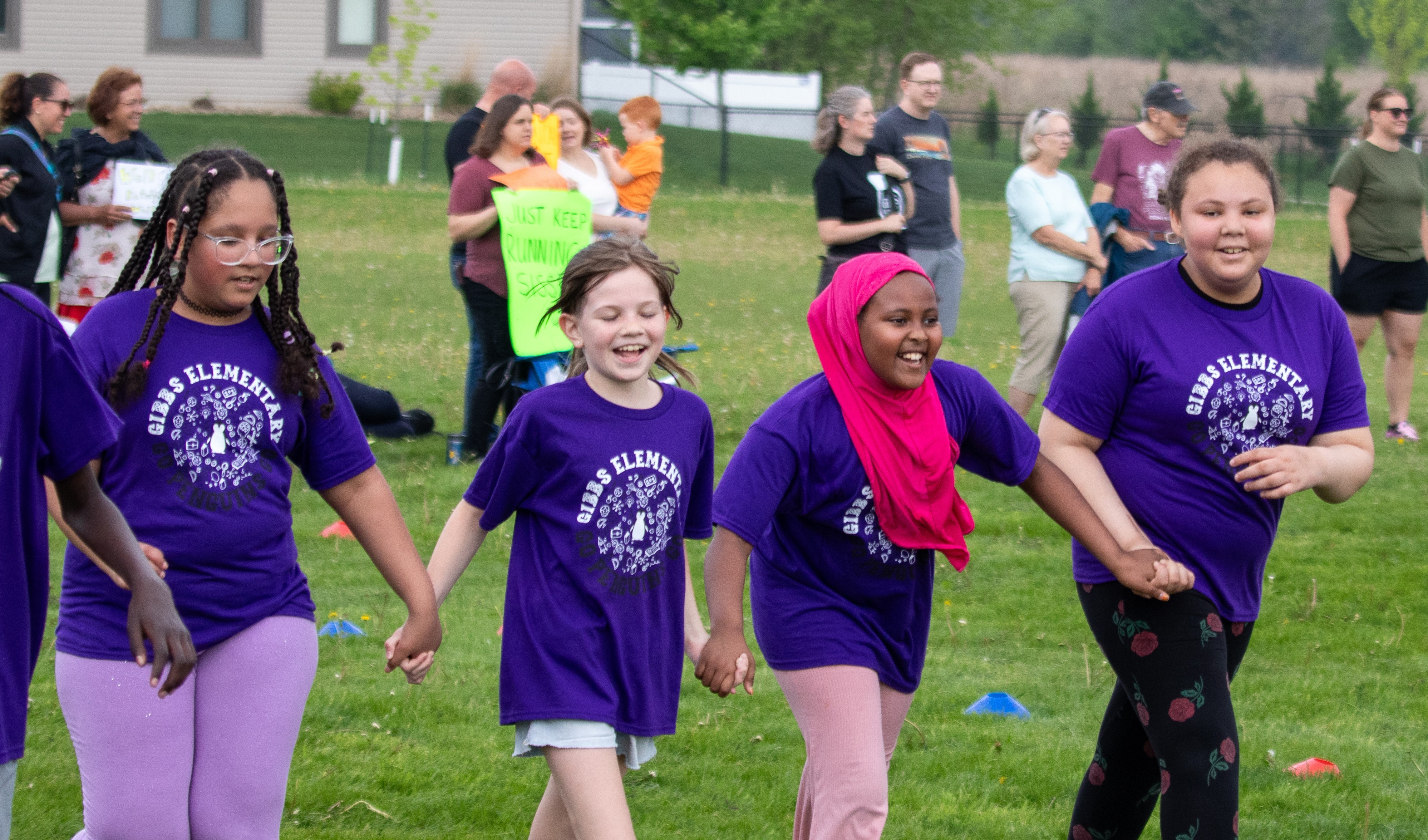 A diverse group of Gibbs student wear matching purple shirts and hold hands at the Gibbs Fun Run.
